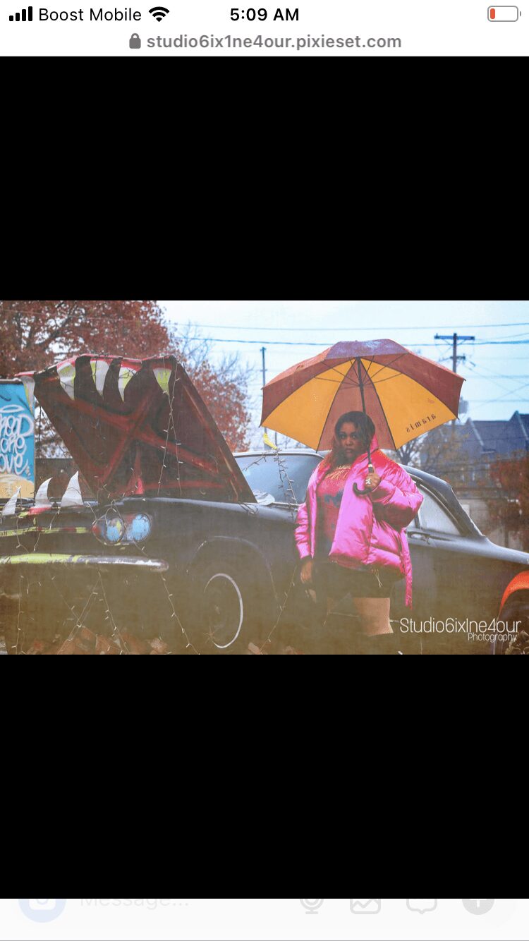 Person holding a yellow umbrella outdoors, wearing a pink jacket, with trees and power lines in background.