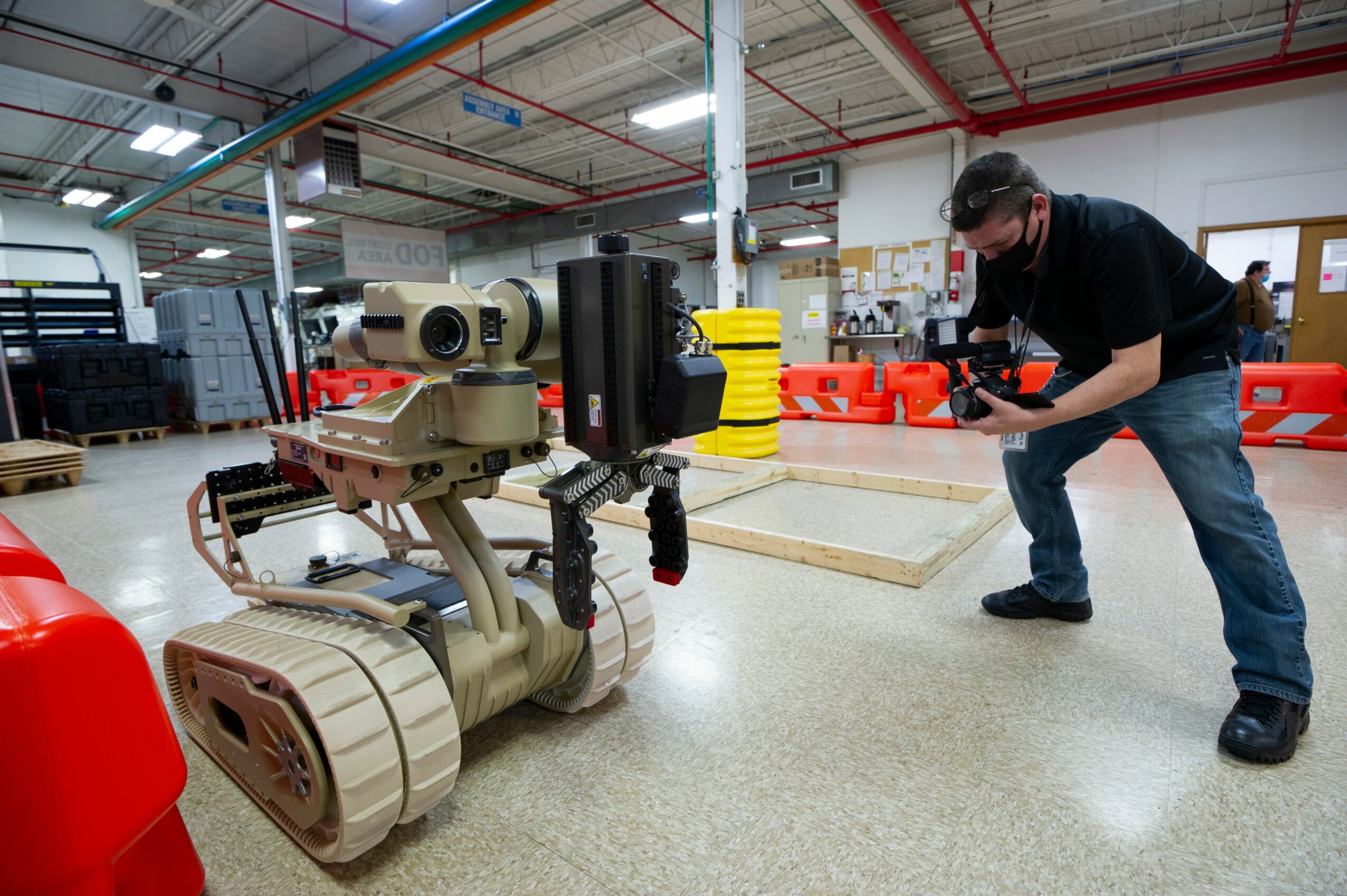 Person operating a robotic device in a workshop with tools and equipment, taking a photo or inspecting the device.