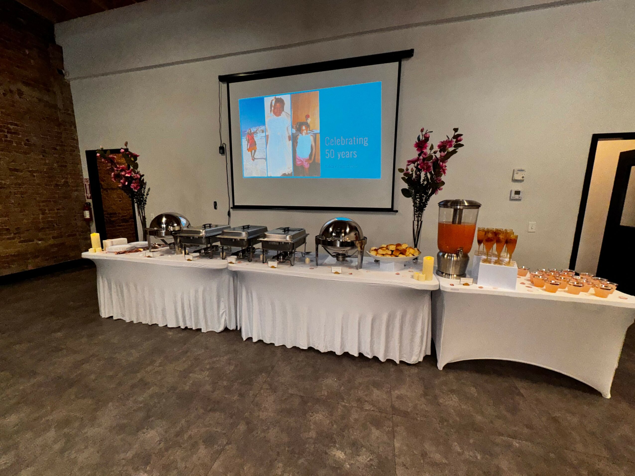 Projection screen displaying a presentation with colorful images and text, flanked by two hanging flower arrangements.