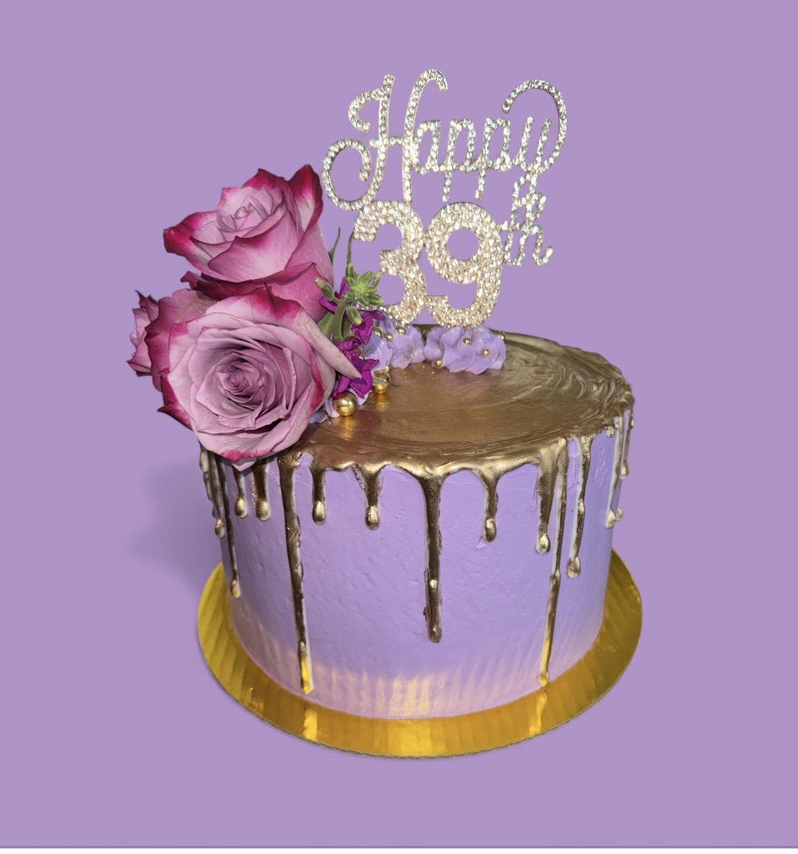 Lavender birthday cake with gold drip, pink roses, and a 'Happy 39th' topper on a purple background.