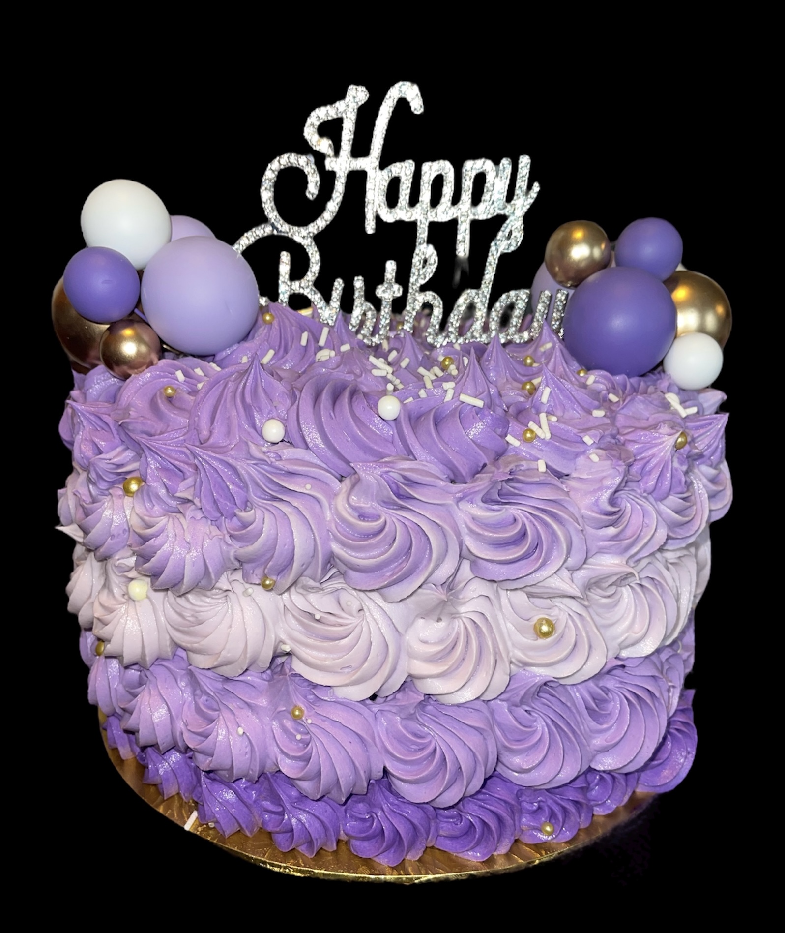 Purple birthday cake decorated with swirls, balloons, and a 'Happy Birthday' topper, against a black background.