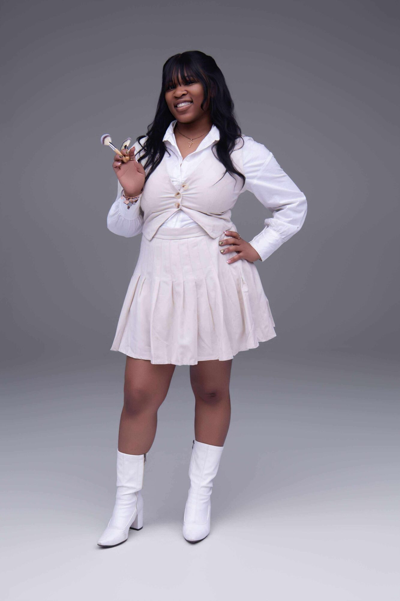 Woman in white dress and boots holding a trophy, smiling, standing against a gray background.