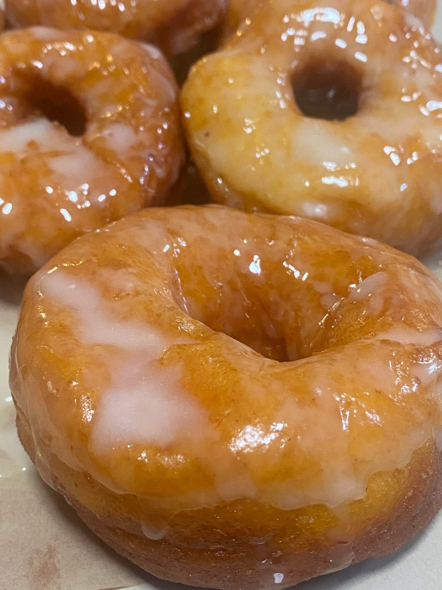 Close-up of glazed donuts with shiny caramel-colored glaze, some with white icing streaks, arranged closely together.