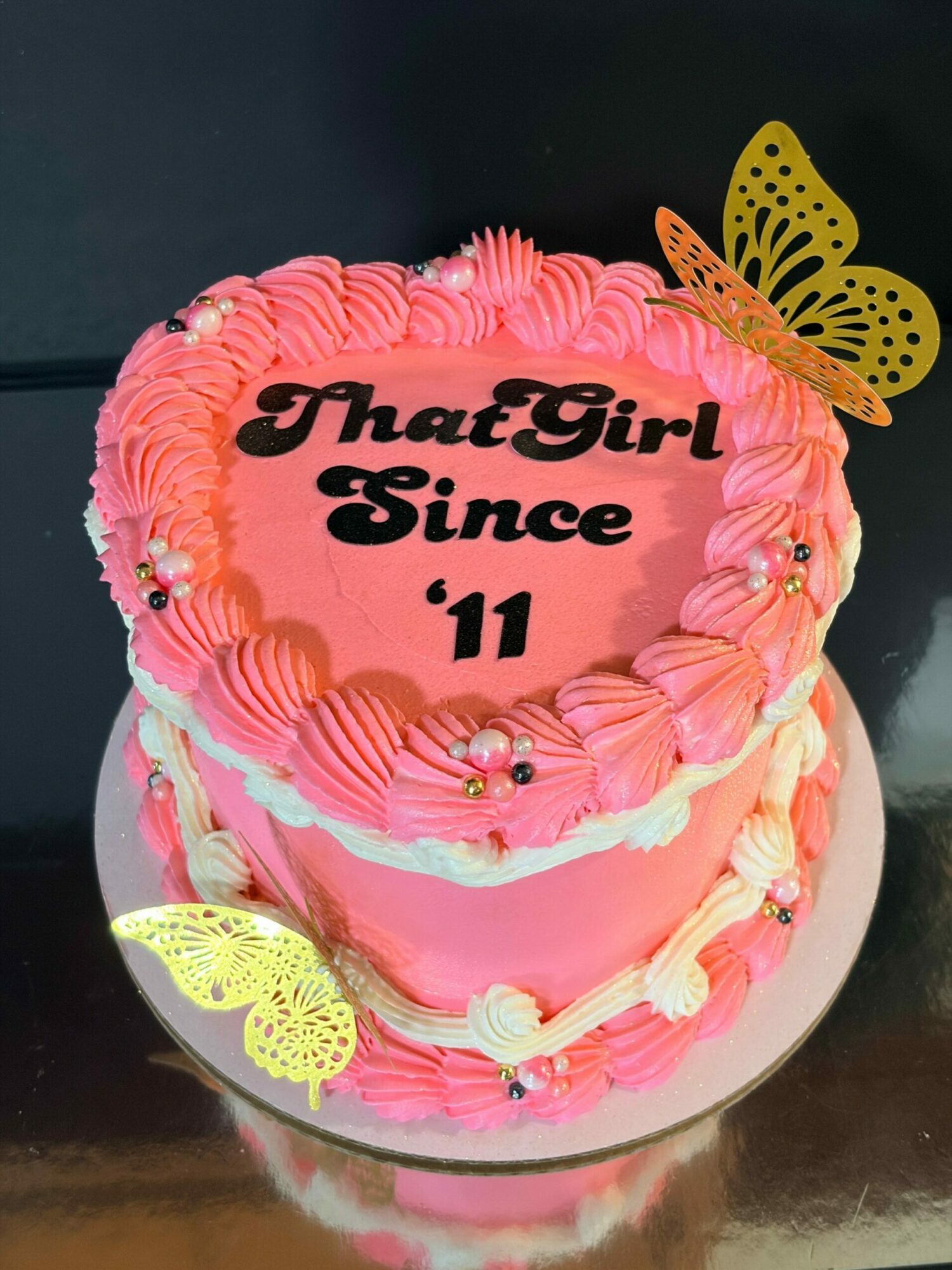 Pink birthday cake with yellow butterfly decorations, decorated with pink and white frosting, and black text reading 'TheaGirl girl 11'.
