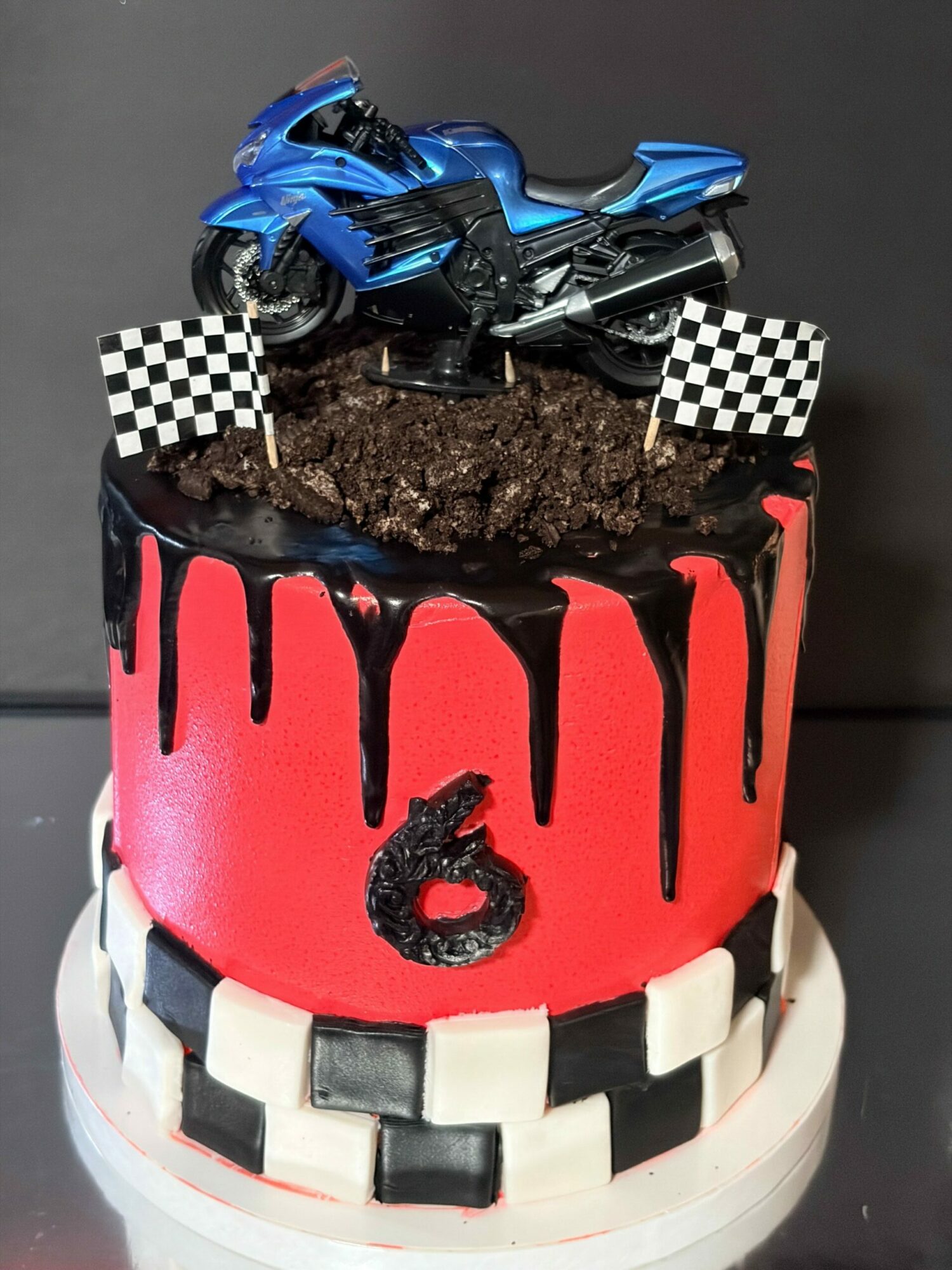 Cake with a motorcycle, checkered flags, and a racing theme, decorated with red, black, and white colors.