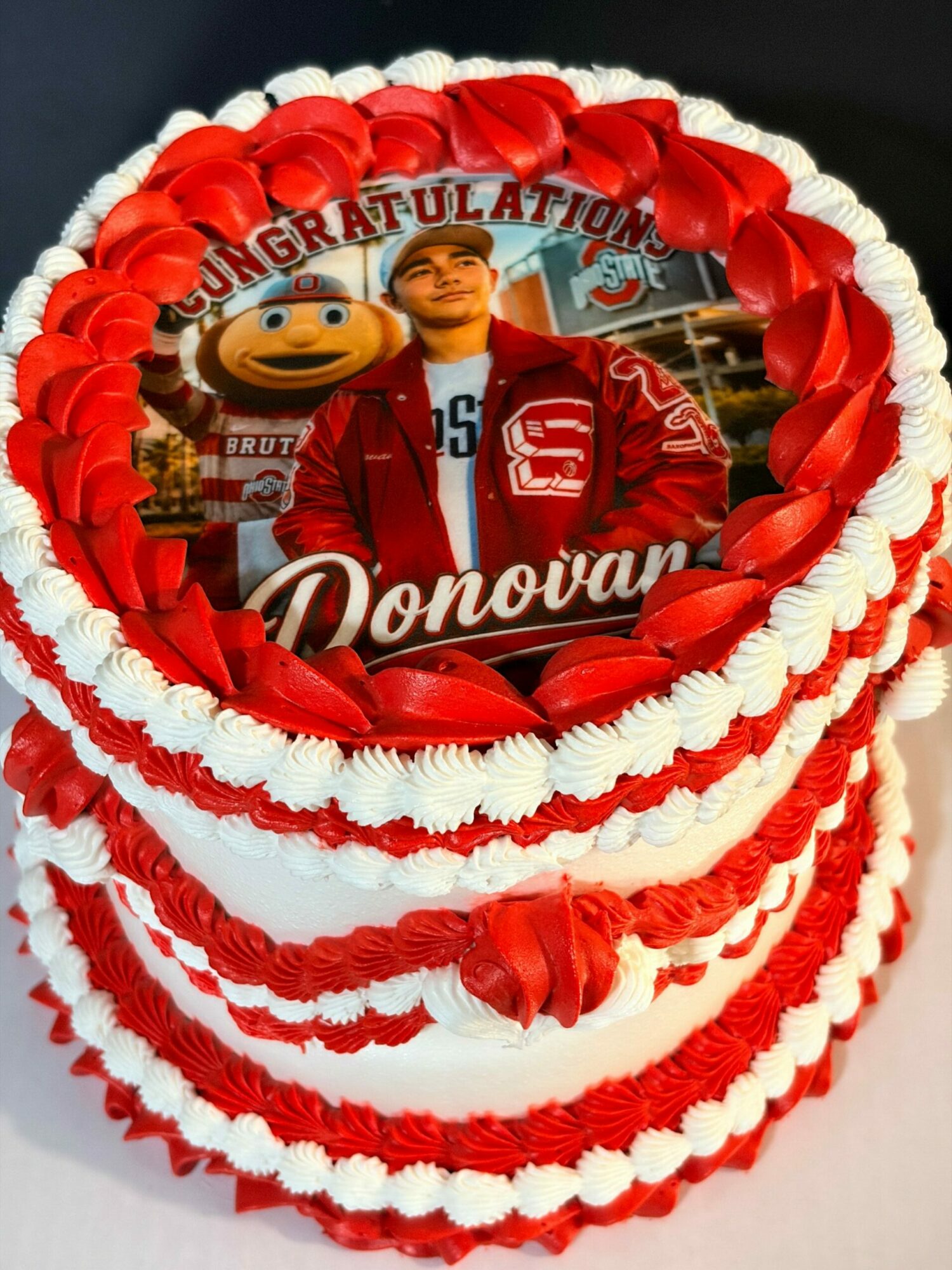 Heart-shaped cake with red and white decorations, featuring a photo of a person in a red jacket inside.