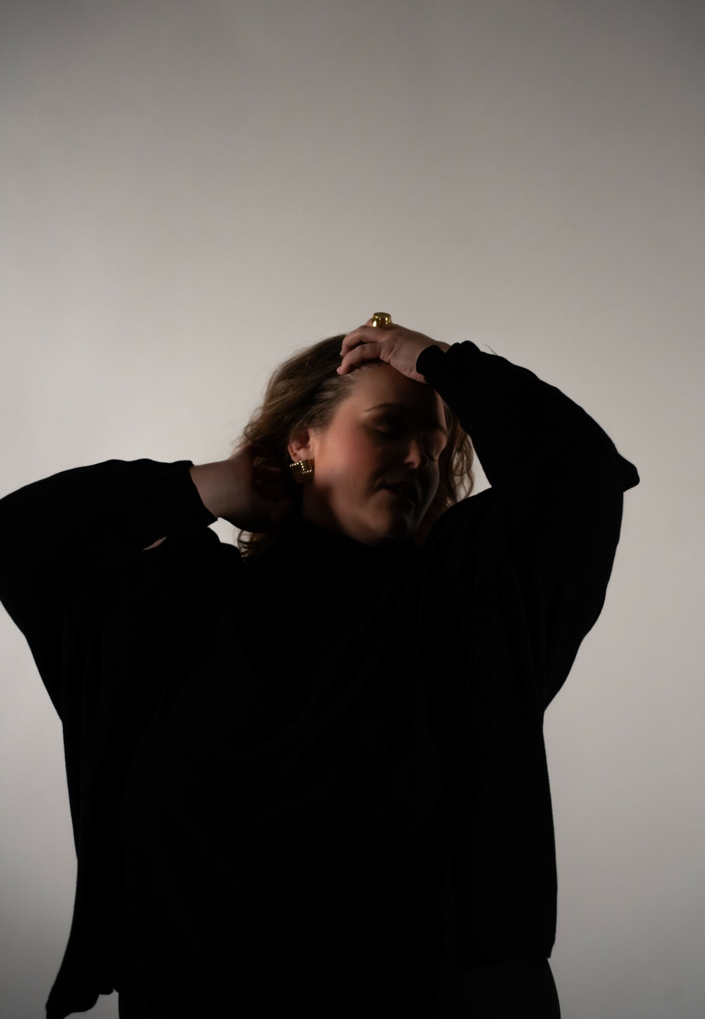 Person with hand on head, wearing dark clothing, against a plain light background.