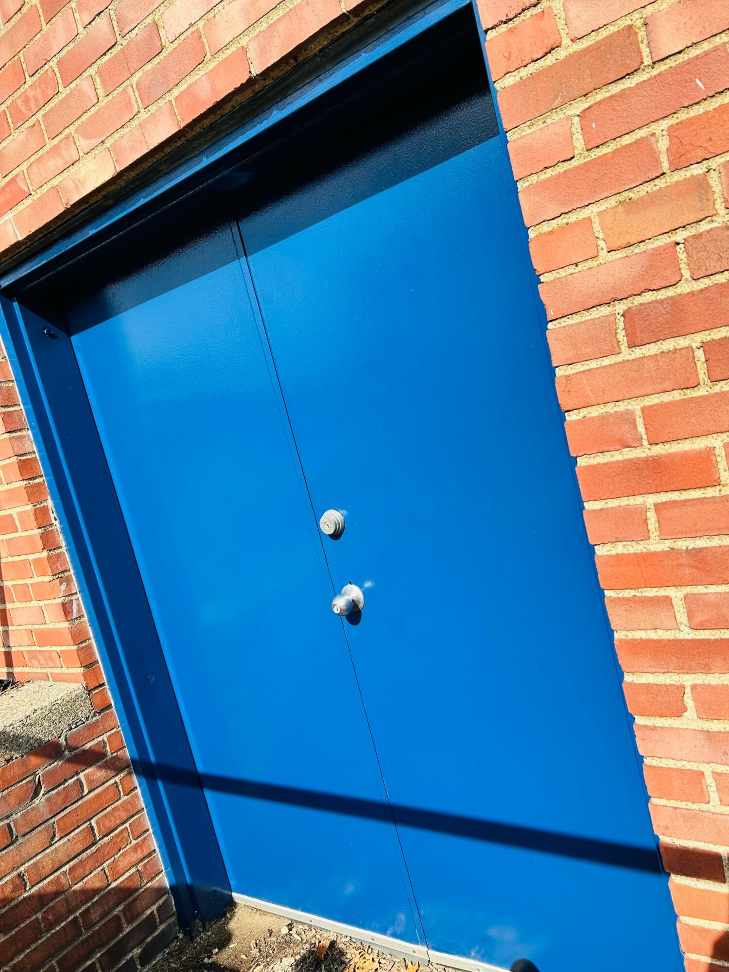 Blue door with a handle and lock, set in a brick wall, slightly tilted, casting a shadow.