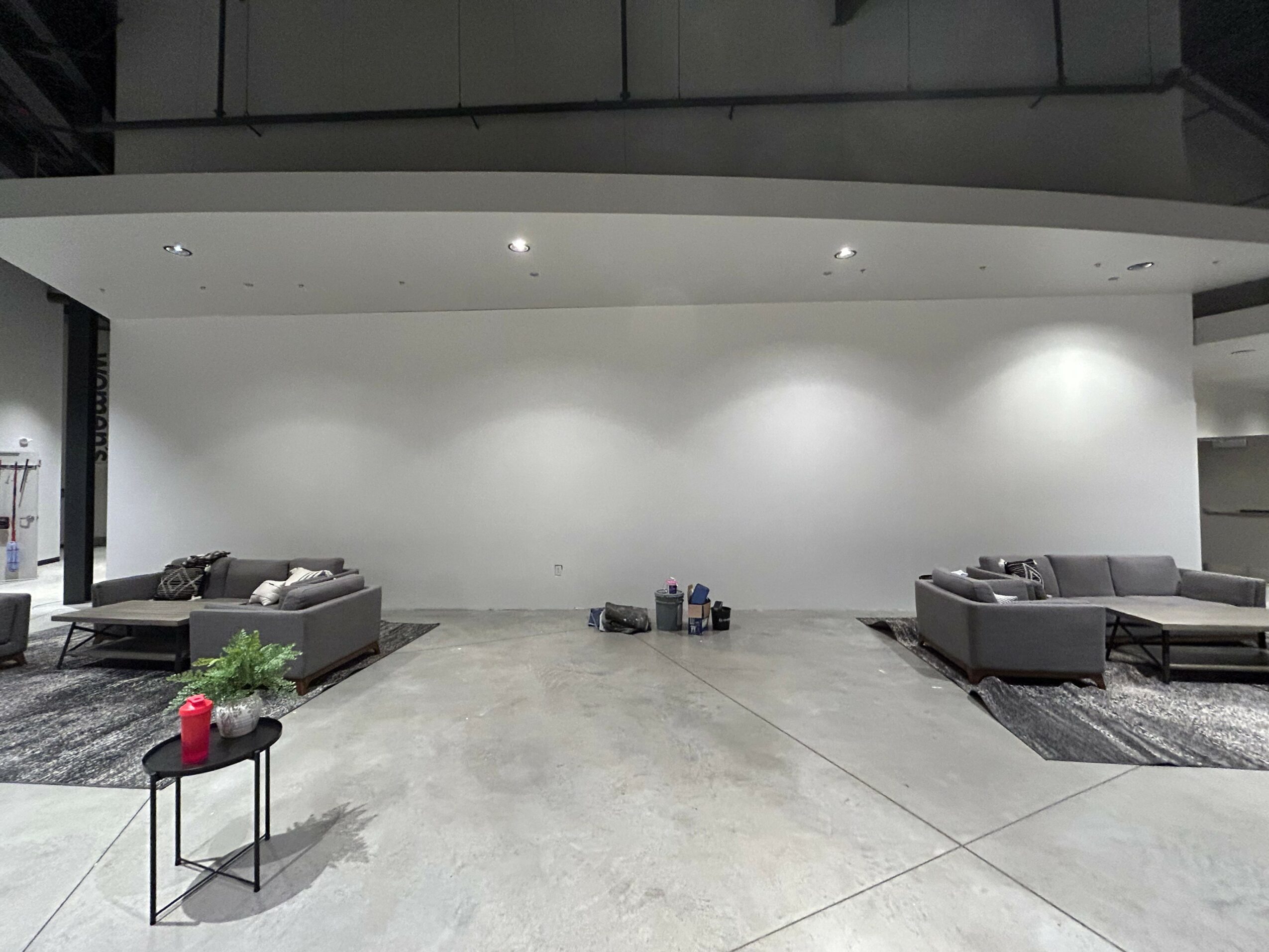 Empty modern lounge with two gray sofas, a small table with a plant and a red object, and a plain white wall.
