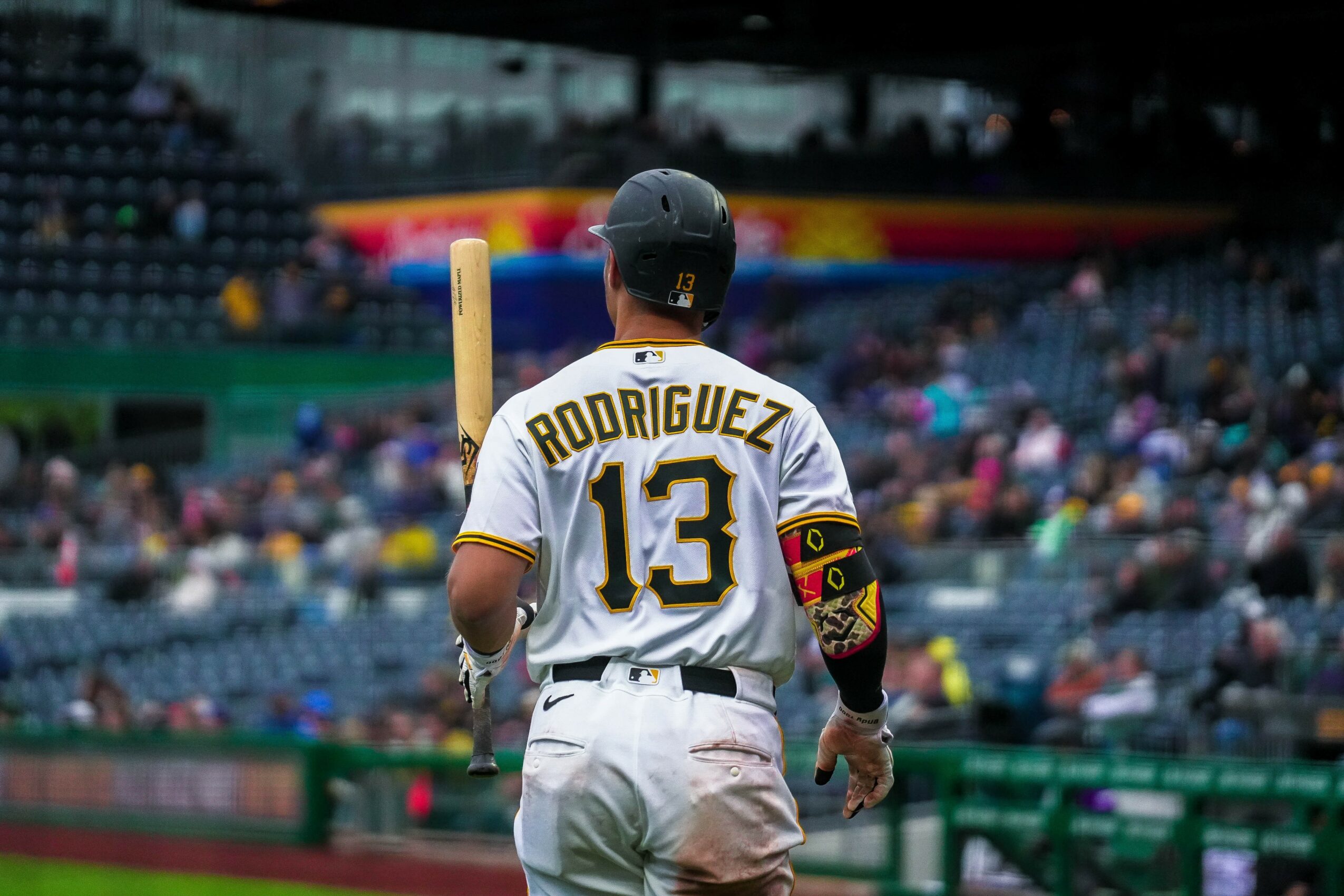 Baseball player with jersey number 13 and name Rodriguez, holding a bat, facing a stadium with spectators.