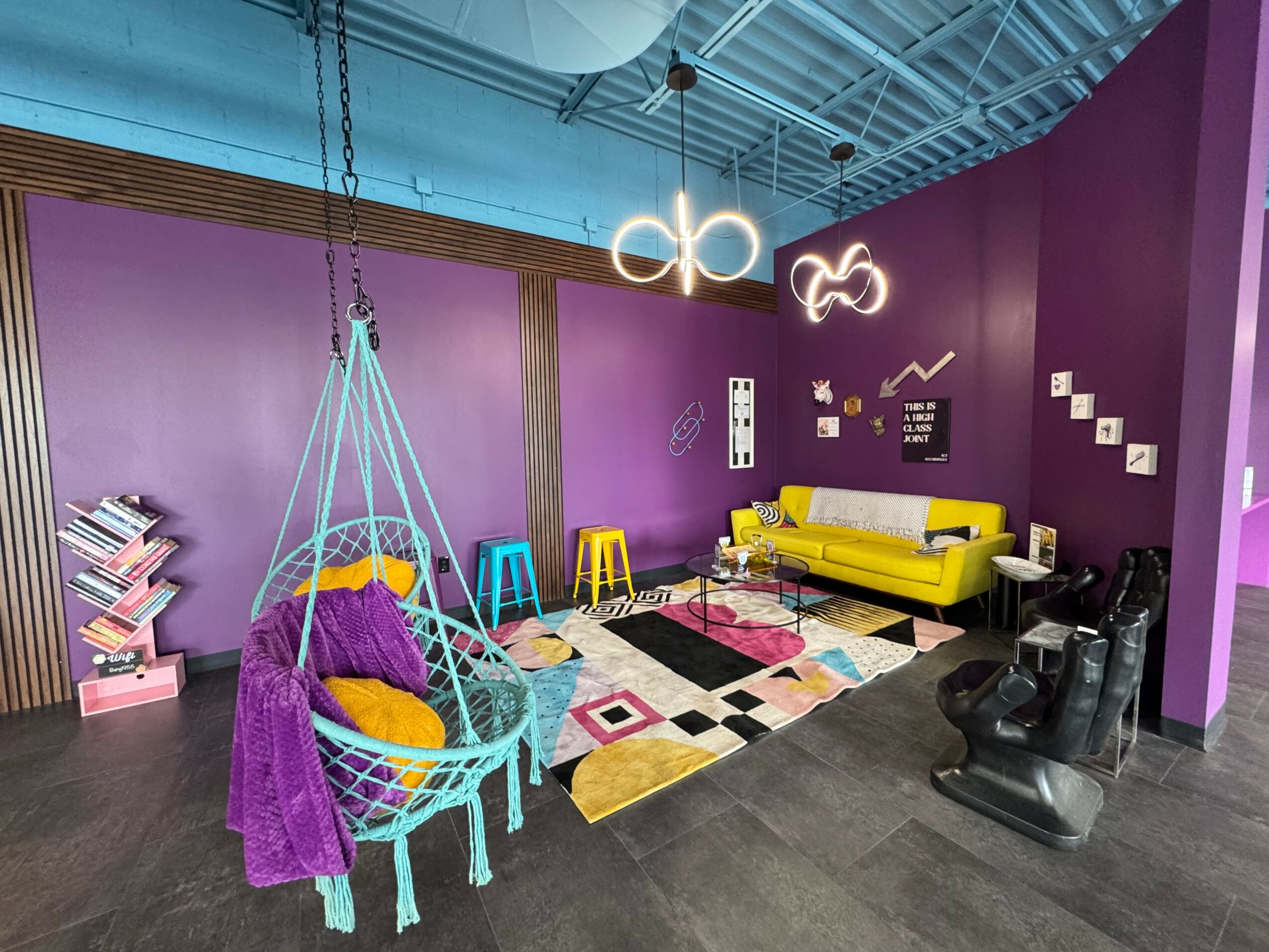 Colorful room with purple walls, hanging swing, yellow sofa, black chairs, and modern lighting fixtures.