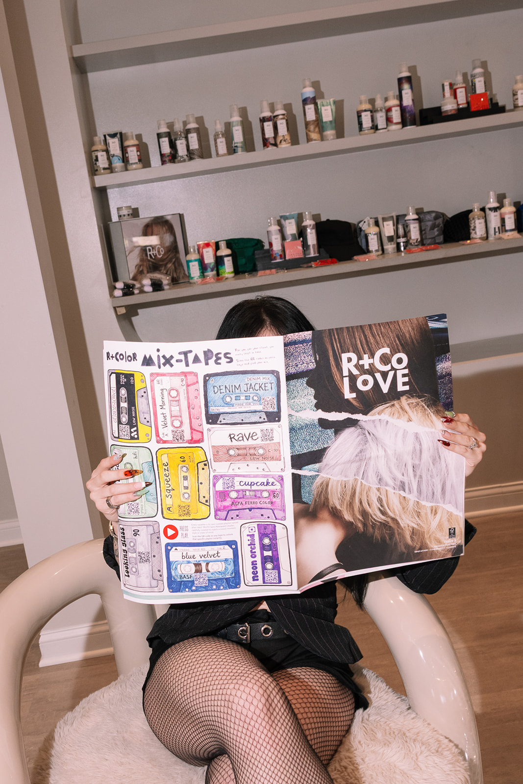 Person sitting in a chair holding a magazine with colorful pages, shelves with bottles in the background.