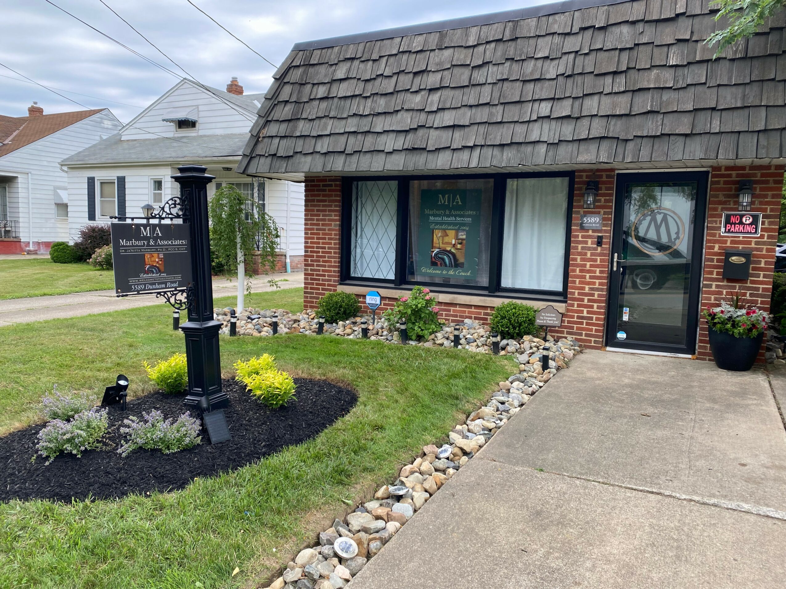 Brick building with large front window, small garden, and sidewalk, in a residential neighborhood.