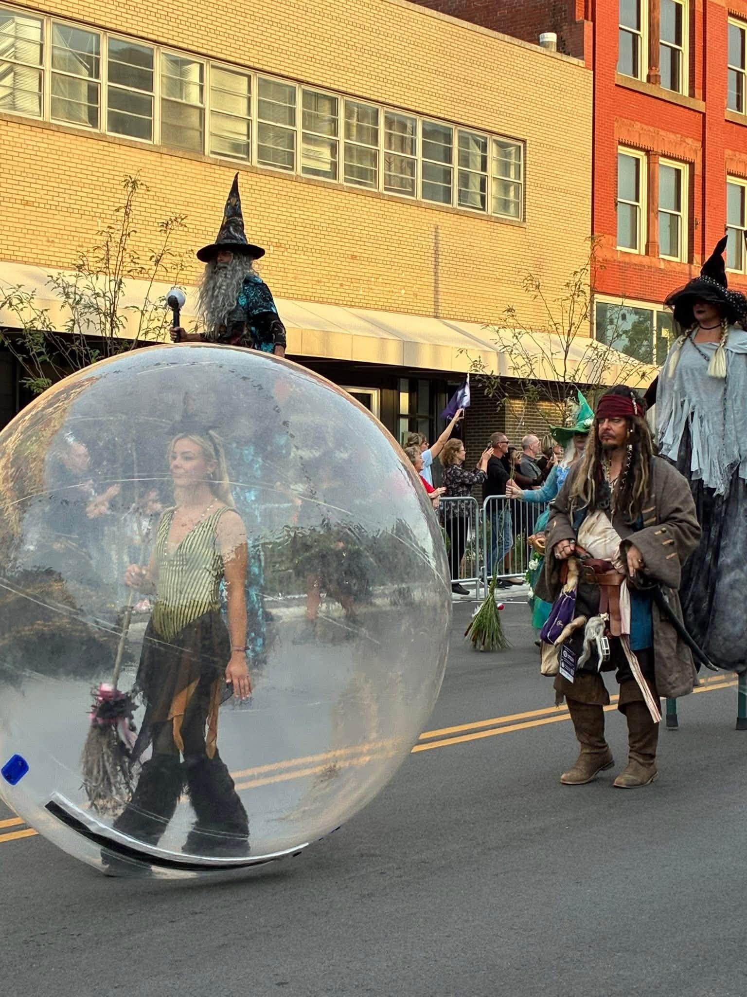 Person inside a transparent sphere on a city street, with people walking nearby and buildings in the background.