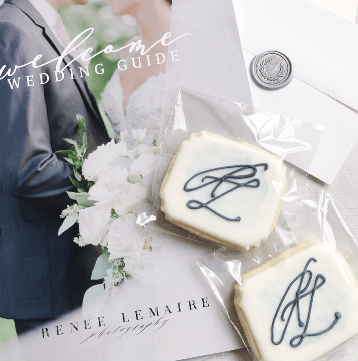 Wedding guide magazine with a wedding cake cookie on top, decorated with a monogram, and a bouquet of white flowers.