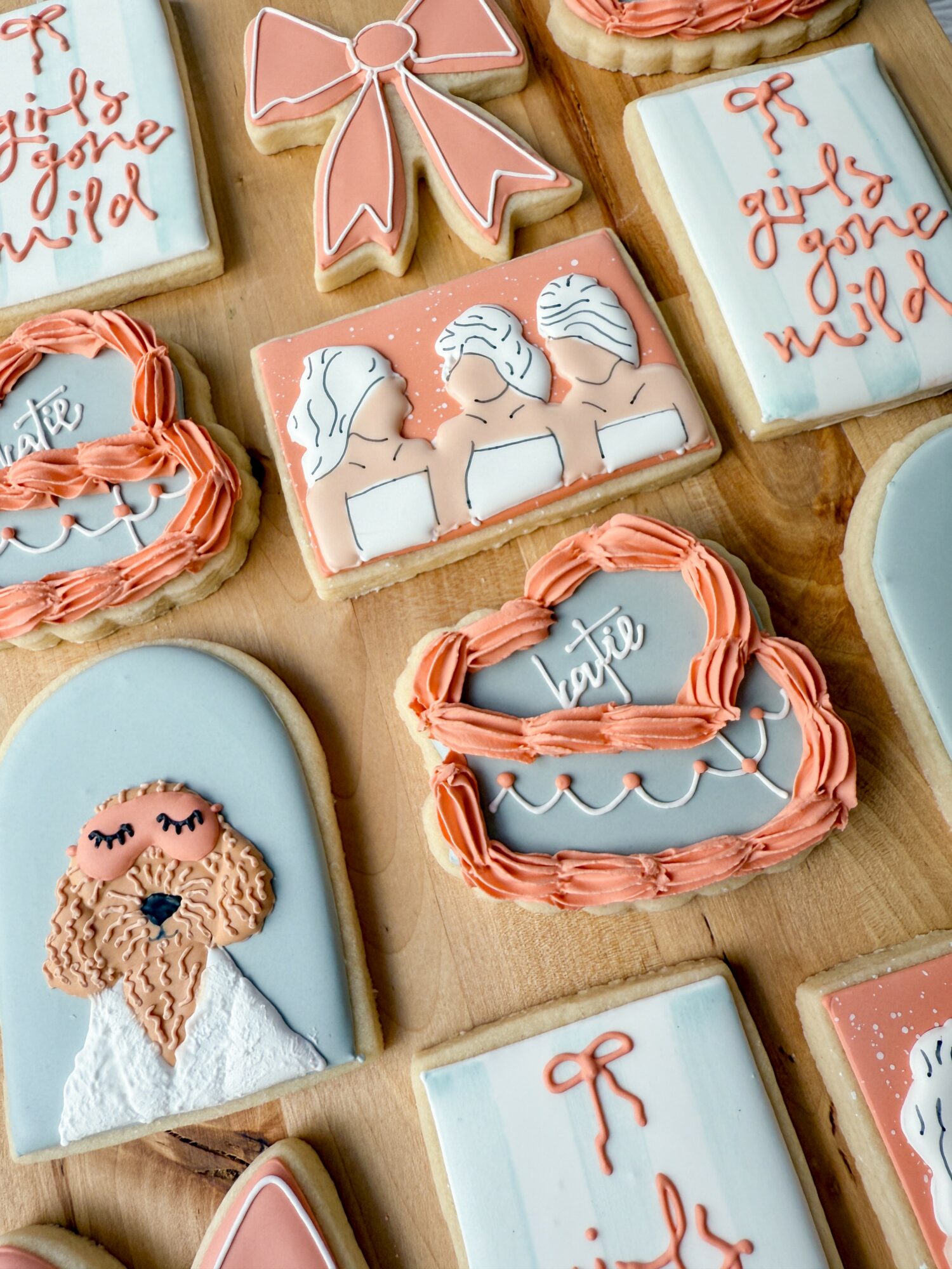 Decorative cookies with pink bows, unicorns, a girl with glasses, and a boat with a bow, arranged on a wooden surface.