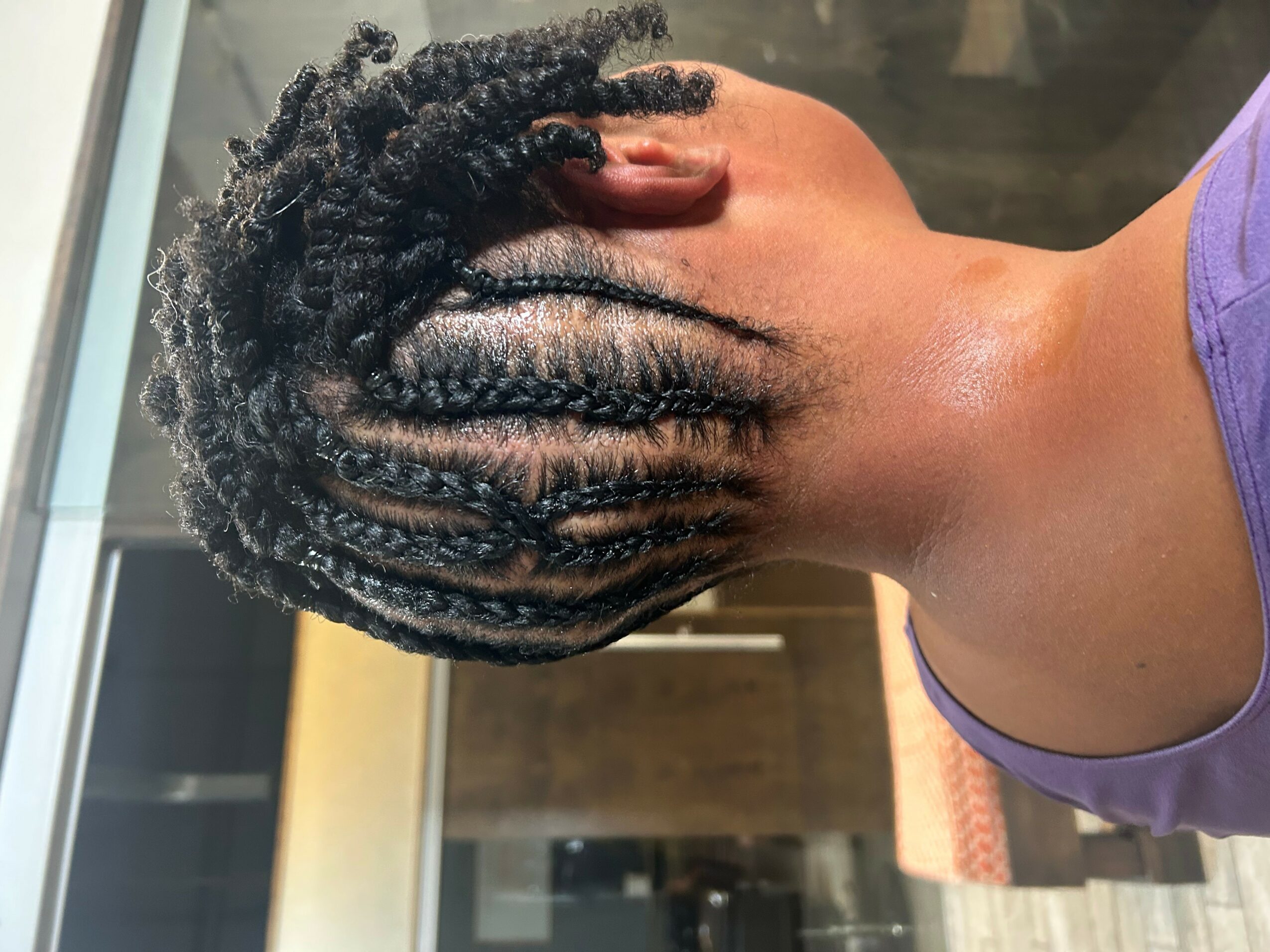 Back of a person's head with styled dreadlocks, wearing a purple top, indoors with a blurred background.