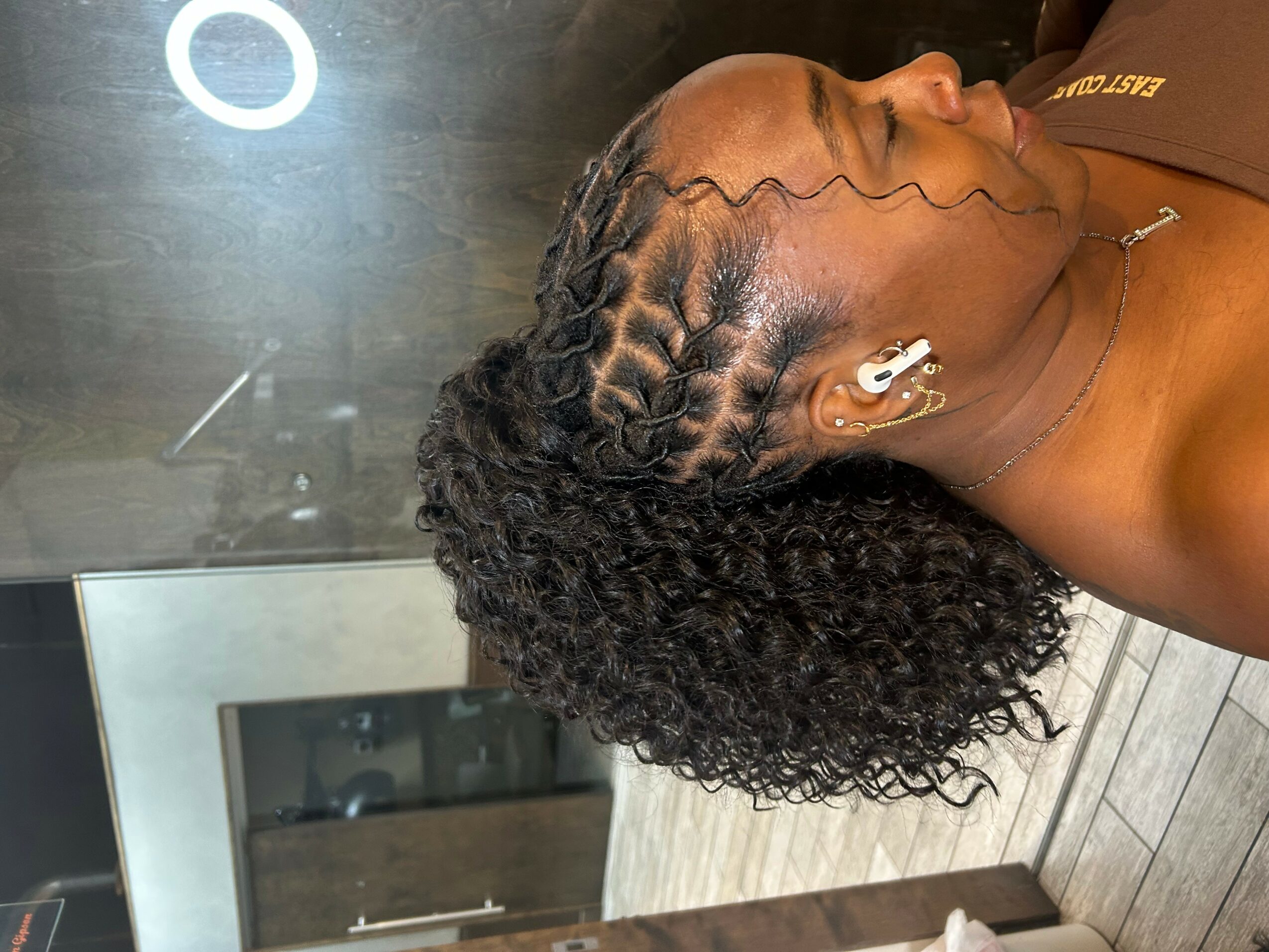 Side view of a woman with curly hair lying down, with braided hair on top, in a room with wooden flooring.