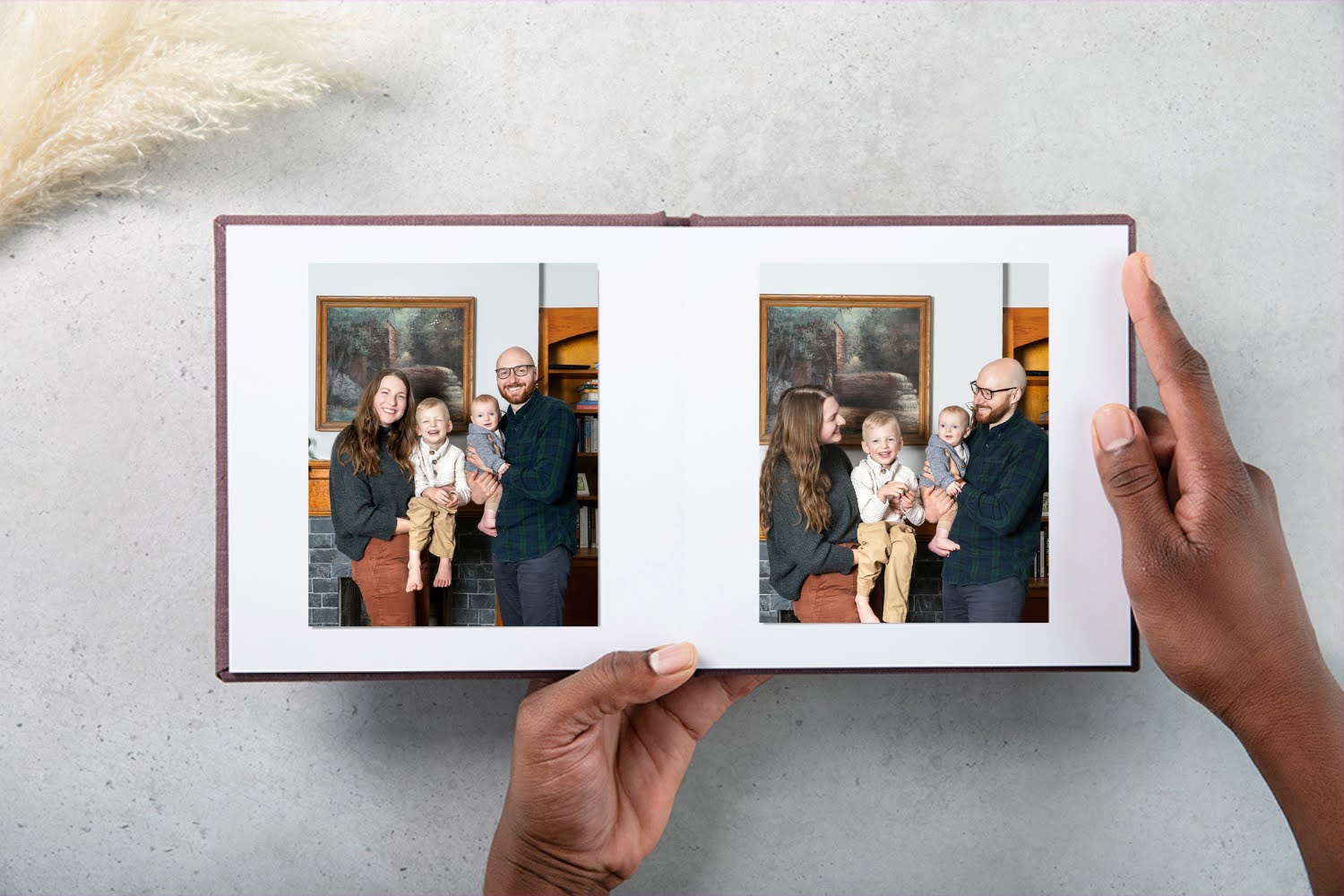 Open photo album showing two pages with family photos, person holding album with right hand, gray background.