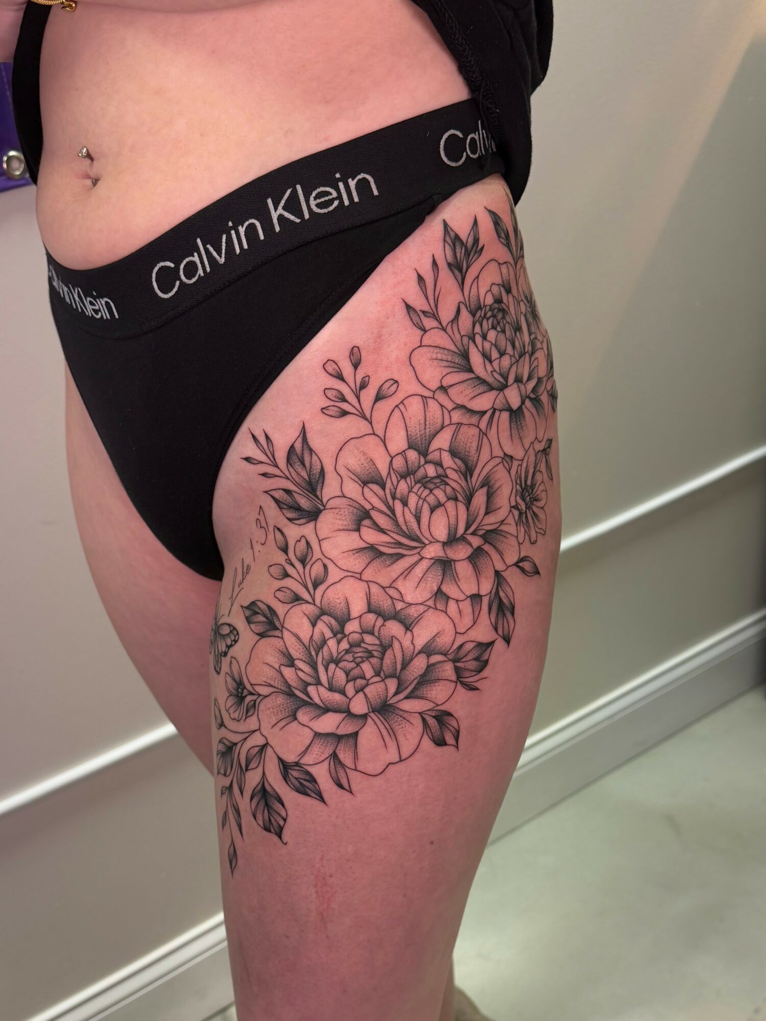 Person wearing black Calvin Klein underwear with floral tattoo on thigh, visible belly button, and light skin tone.