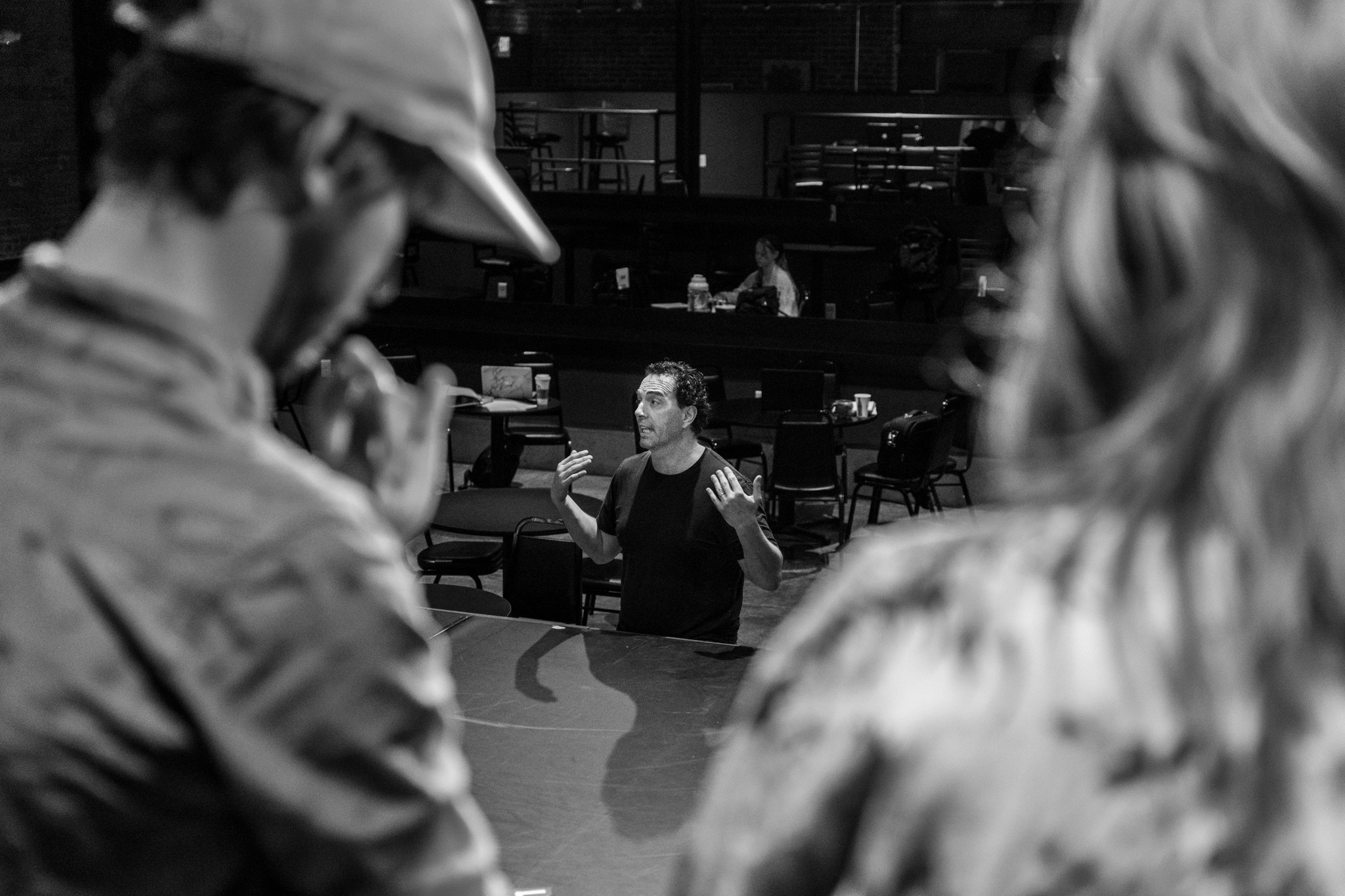 Three people in a conversation, with one person speaking and two others listening, in a dimly lit indoor setting.