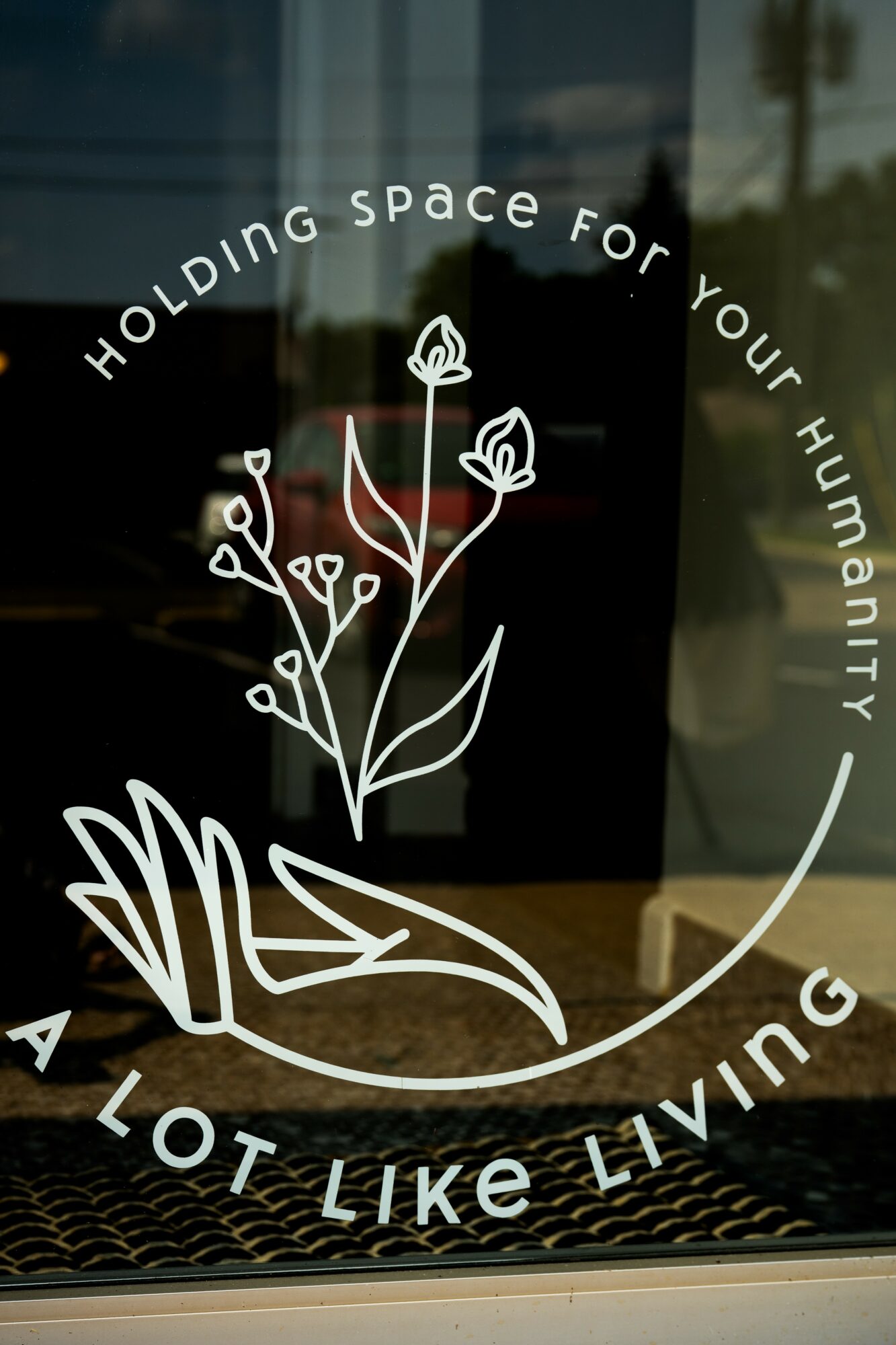 White line drawing of a hand holding a plant with flowers, surrounded by text about holding space and living.