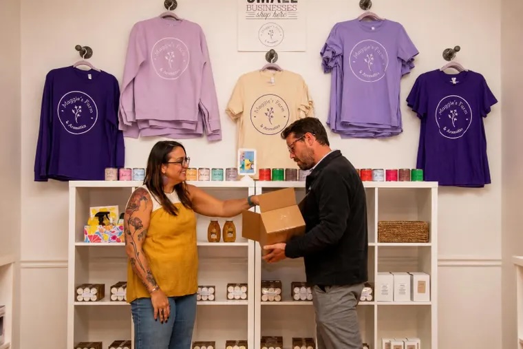 Two people exchanging a box in a store with colorful sweatshirts hanging on the wall behind them.