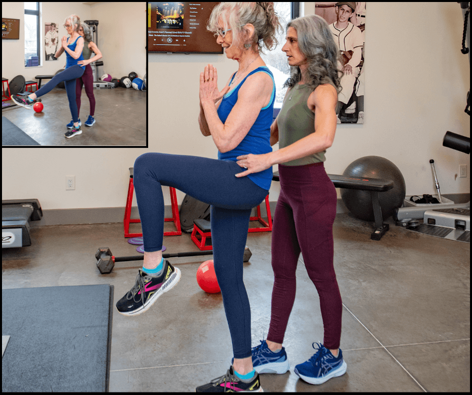 Two women exercising in a gym, one balancing on a step with a knee raise, the other assisting. Gym equipment visible.