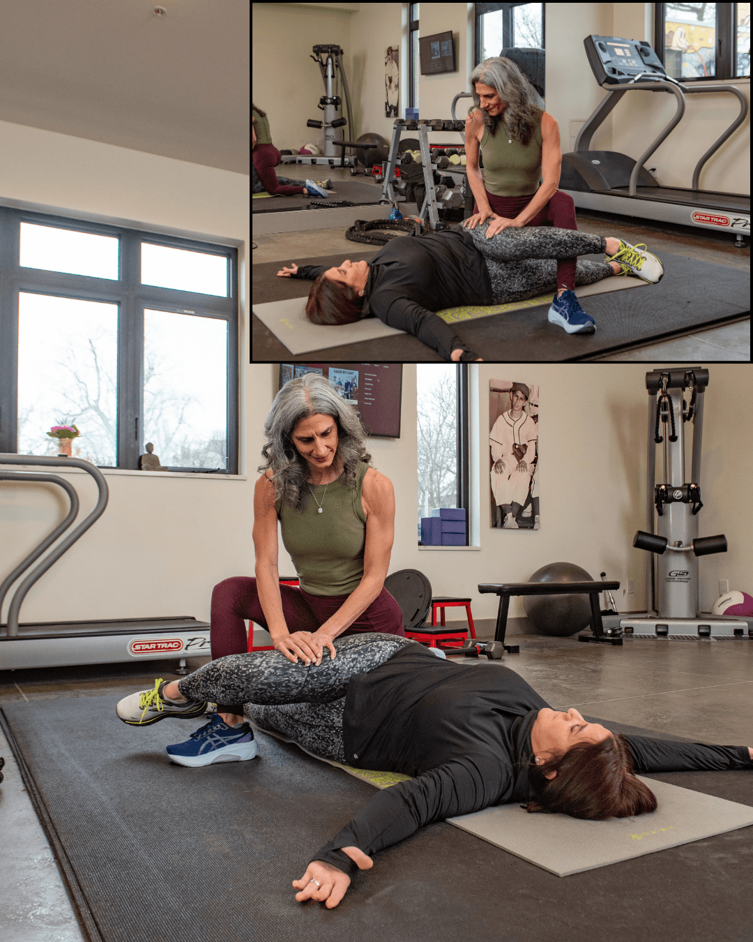 Two women in a gym, one lying on the floor and the other kneeling beside her, performing a stretching exercise.