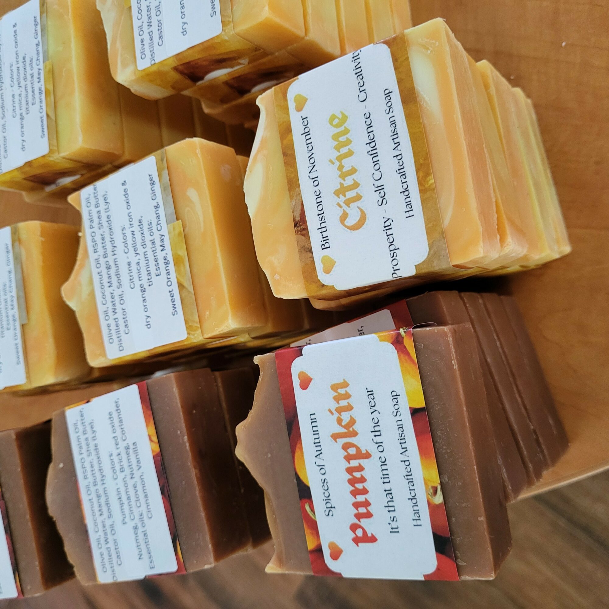 Stacks of soap bars, yellow and brown, with labels, on a wooden surface.