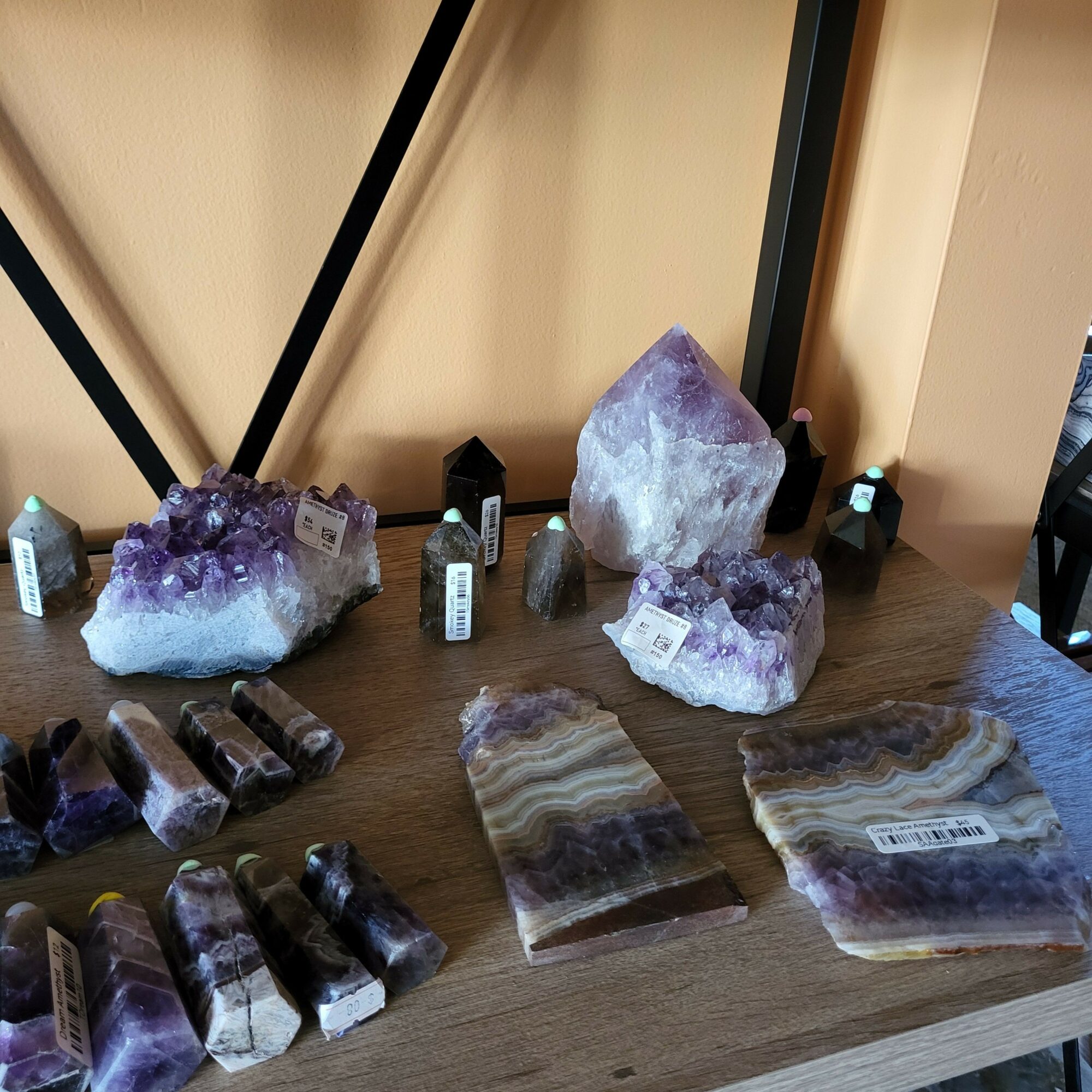 Various amethyst and mineral stones on a wooden table, some with labels, in a room with beige walls.