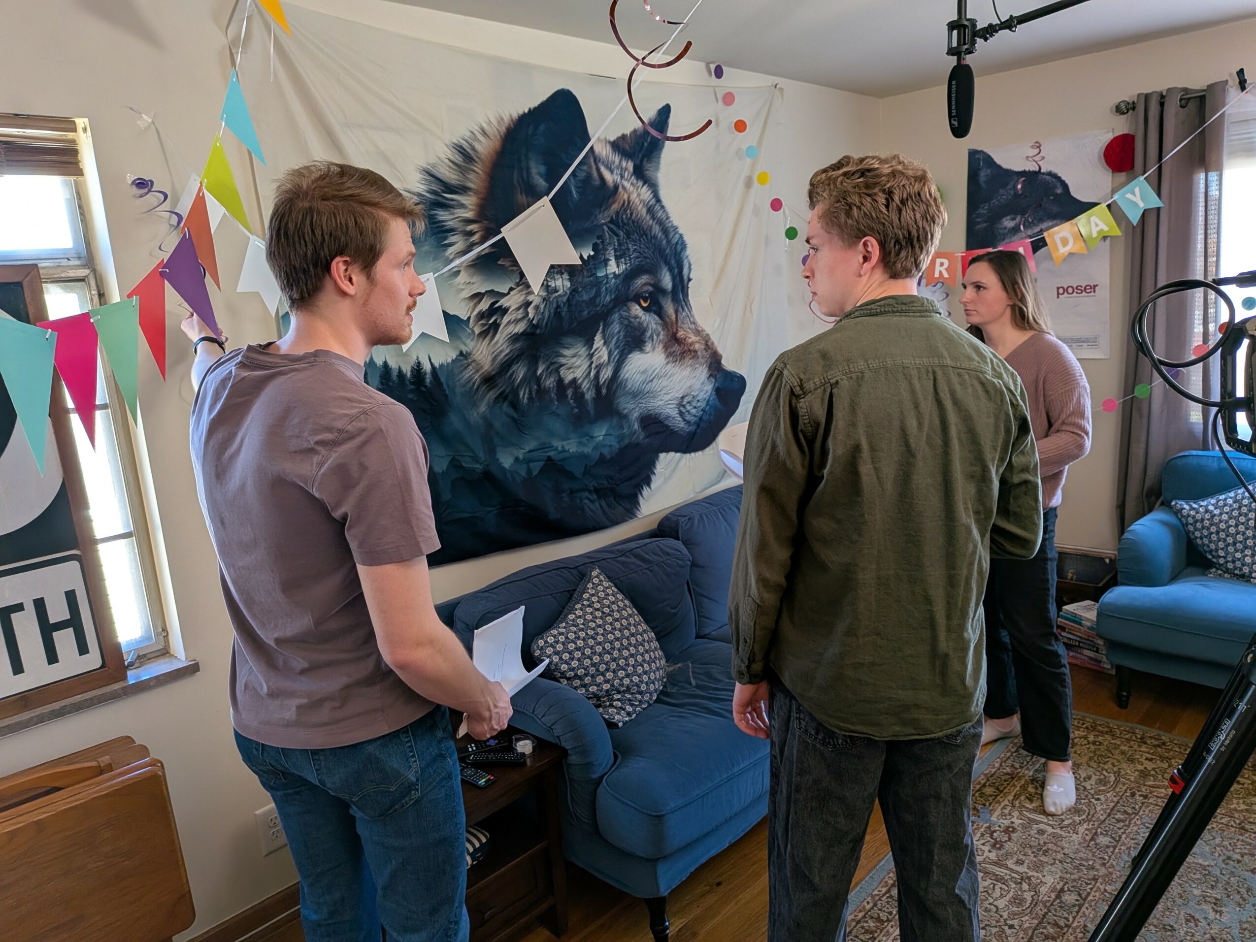 Three people in a room with a large wolf mural on the wall, colorful decorations, and furniture including a blue sofa.