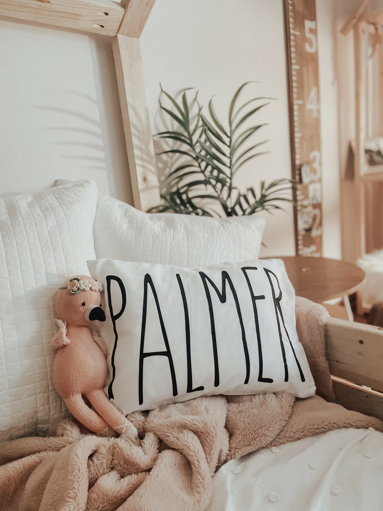 A cozy scene with a pillow labeled 'PALMER', a teddy bear, and a plant in the background.