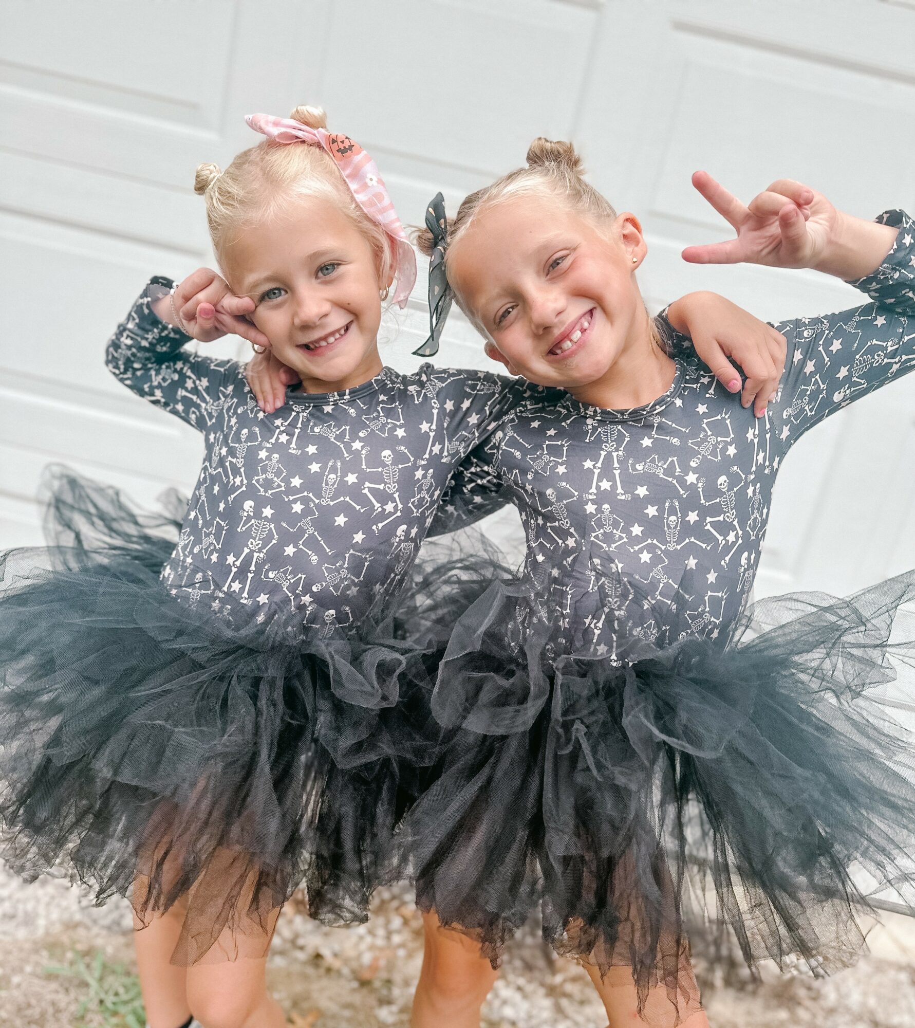 Two young girls in matching star-patterned dresses and black tutus, smiling and posing with arms around each other, indoors.