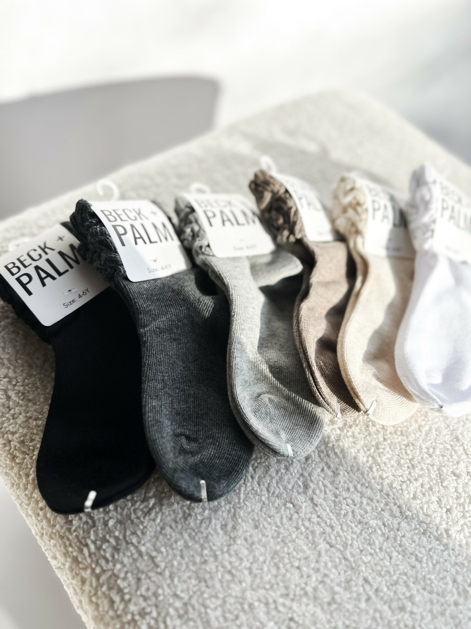 Six pairs of socks in black, dark gray, light gray, beige, and white are arranged on a textured surface.