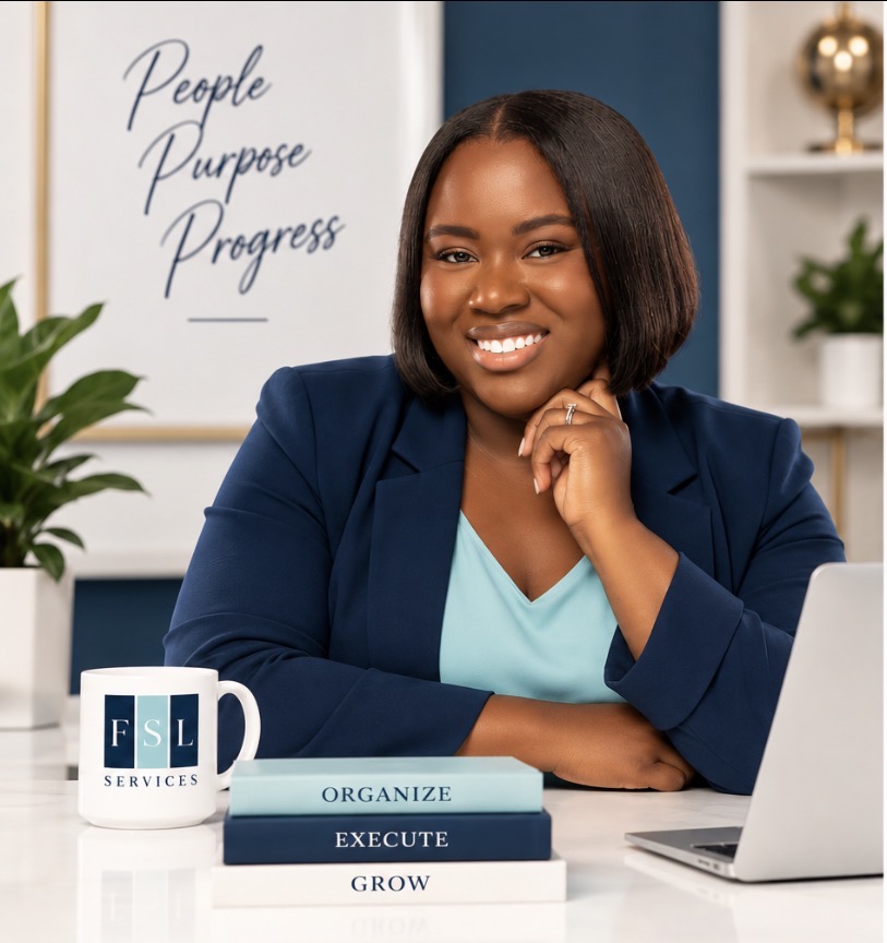 Smiling woman in blue blazer sitting at desk with laptop and books, in a modern office setting.