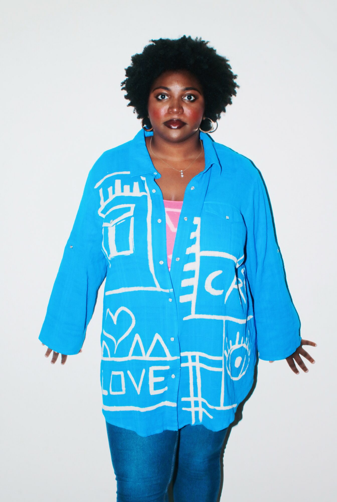 Woman with curly hair wearing a blue jacket with white graphic designs, standing against a plain background.