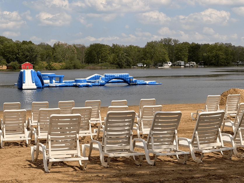 Beach chairs facing a lake with an inflatable water slide on the water, trees in the background, and a partly cloudy sky.