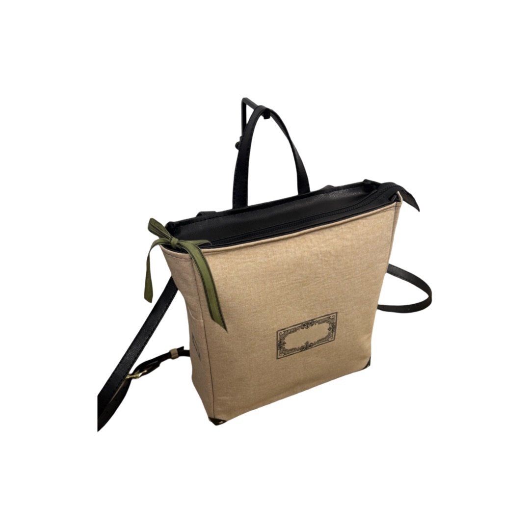 Beige bag with black zipper, handle, and shoulder strap, featuring a green ribbon detail, isolated on white background.