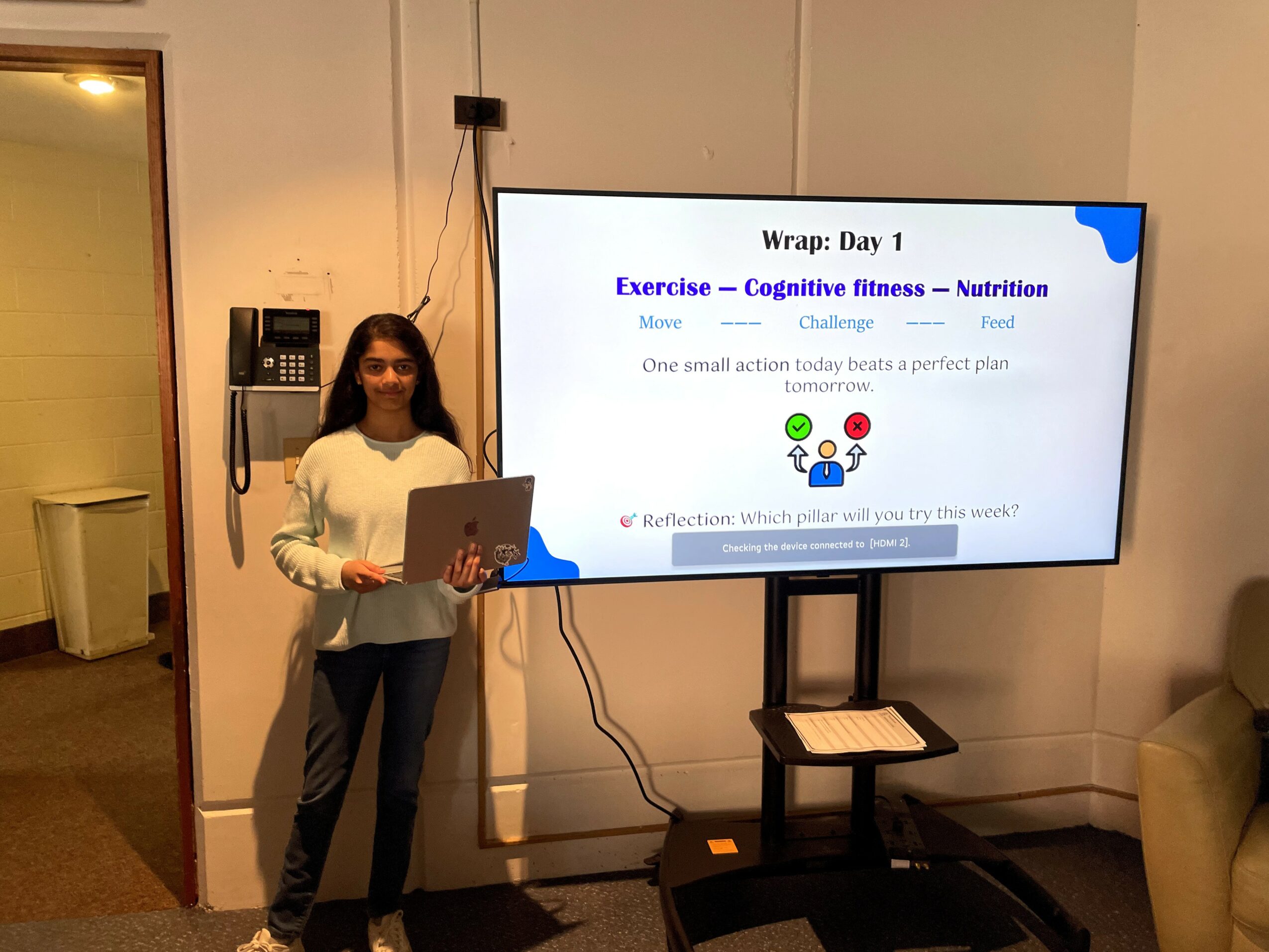 Girl standing next to a large screen displaying a presentation slide about exercise and nutrition.