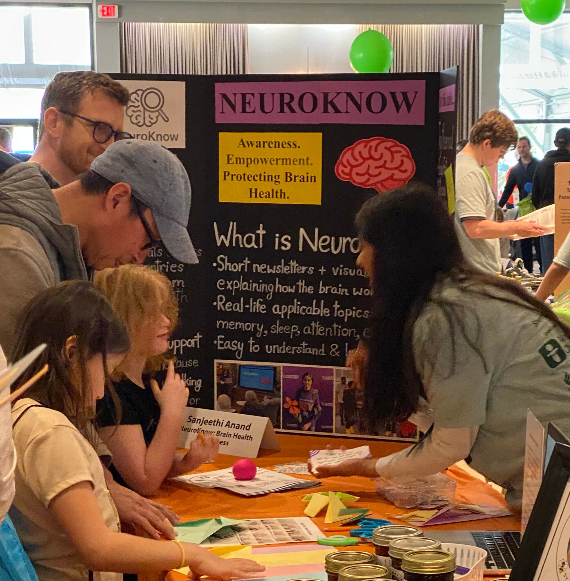 People gathered around a table at a neuroscience event, with a colorful poster about the brain in the background.