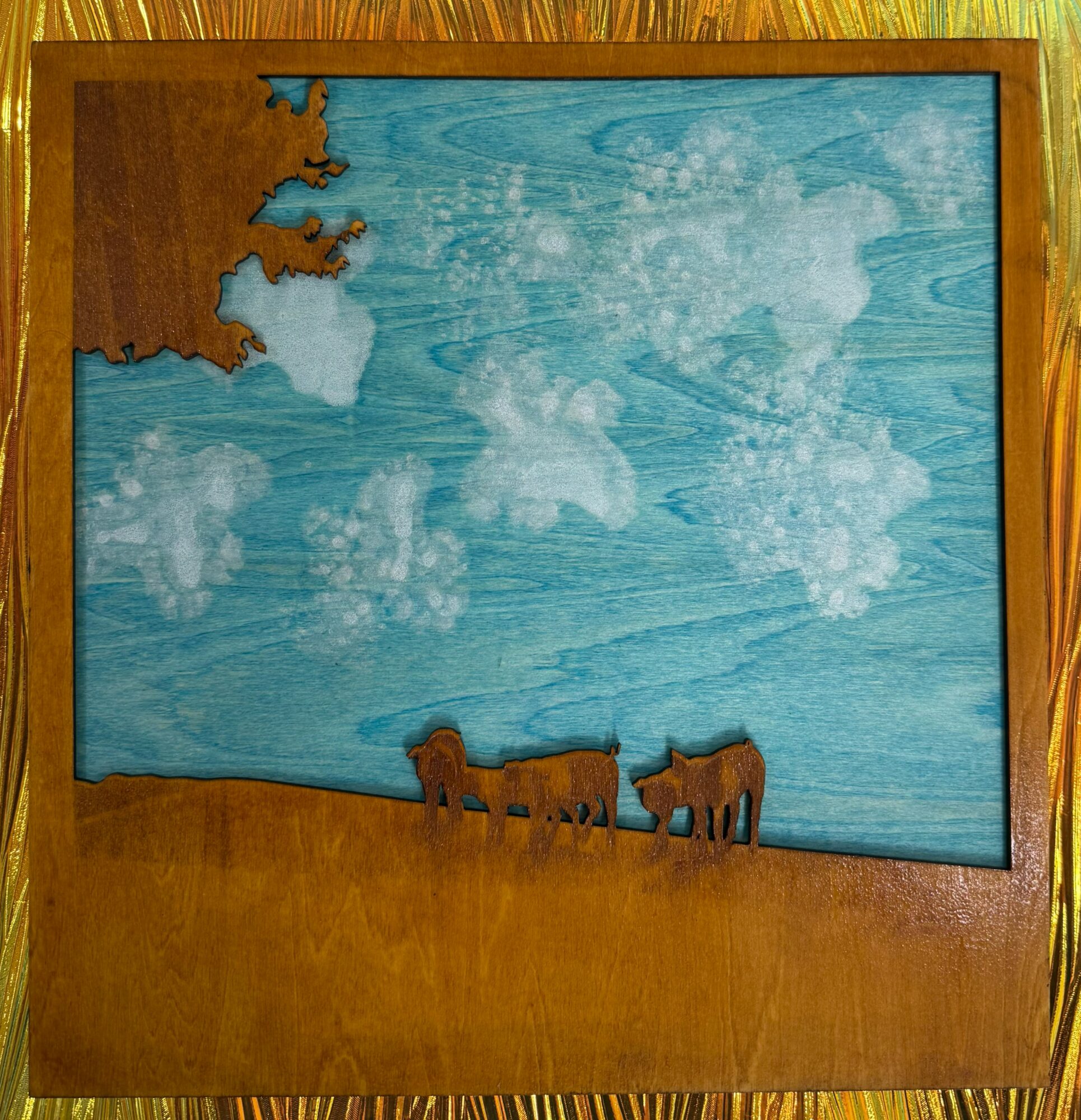 Wooden framed artwork depicting a blue sky with clouds and two animals on a brown ground.
