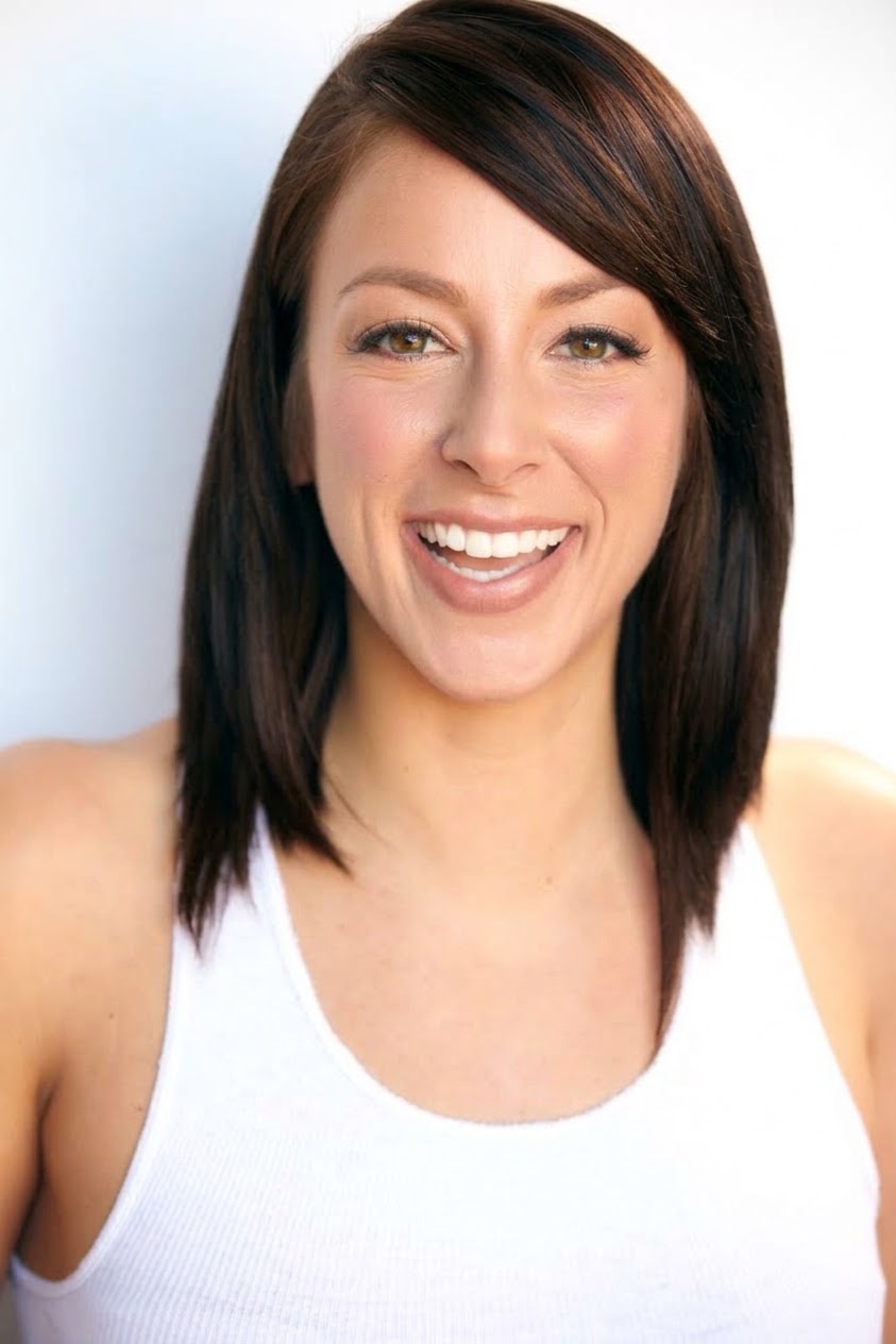 Smiling woman with shoulder-length dark hair wearing a white tank top, facing forward, light background.