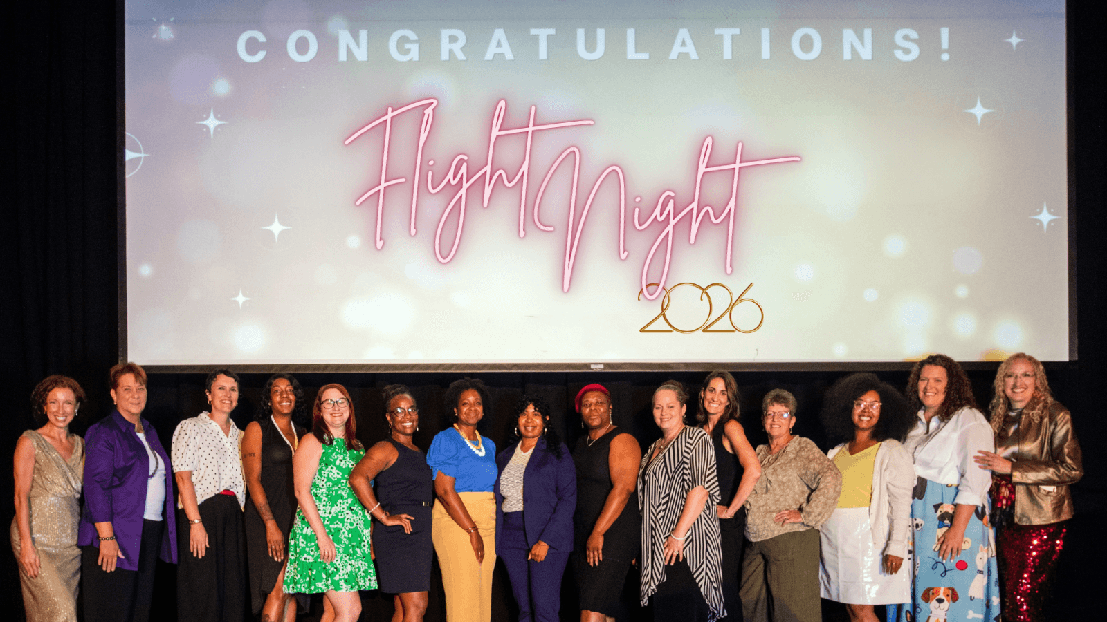Group of people standing in front of a screen with congratulatory message for Flight Night event, 2023.