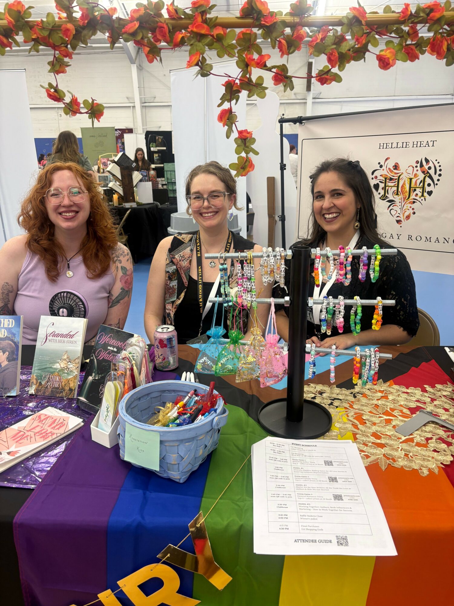 Two women standing behind a table with birthday cakes and decorations, celebrating indoors with colorful tablecloths and flowers.