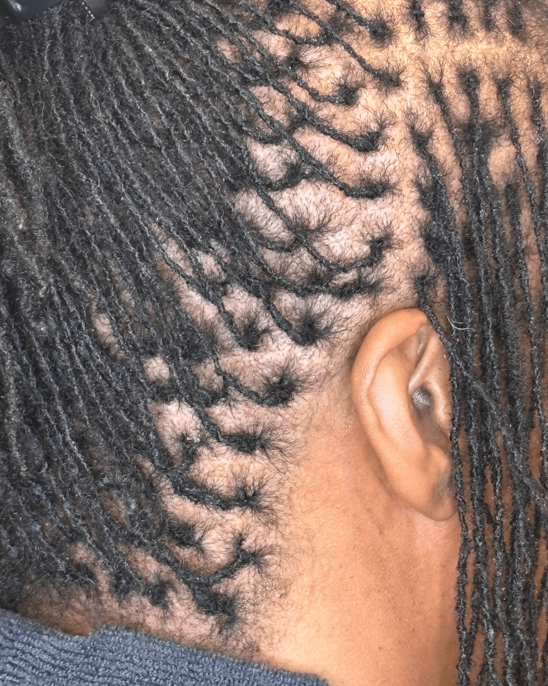 Close-up of a person's head showing styled dreadlocks and a shaved section near the ear.