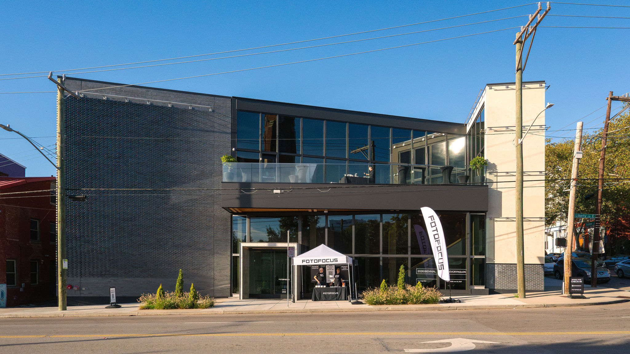 Modern two-story building with glass windows, a small tent, and a flag outside on a sunny day.