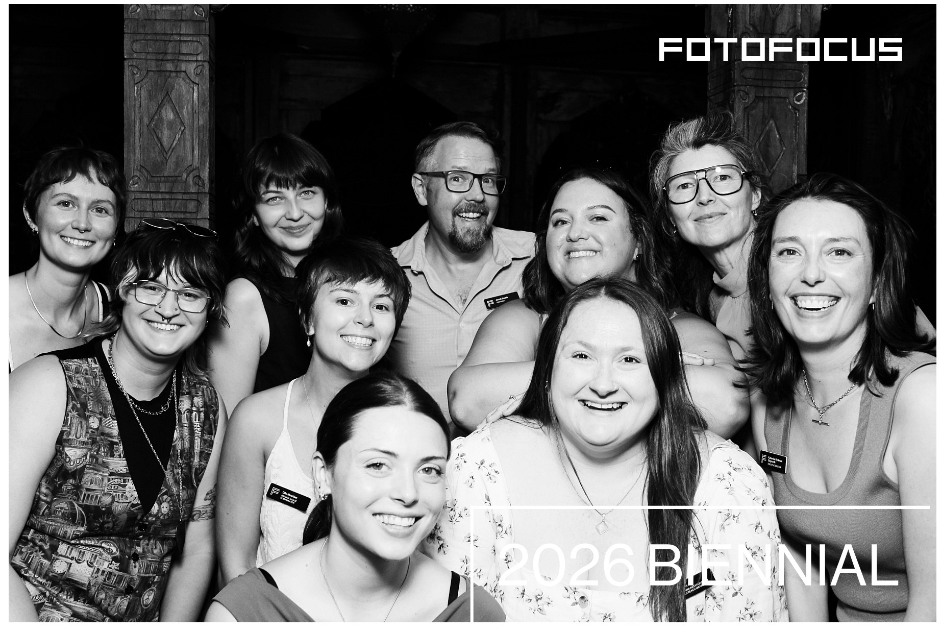 Group of ten smiling people posing indoors, some wearing glasses, in black and white.