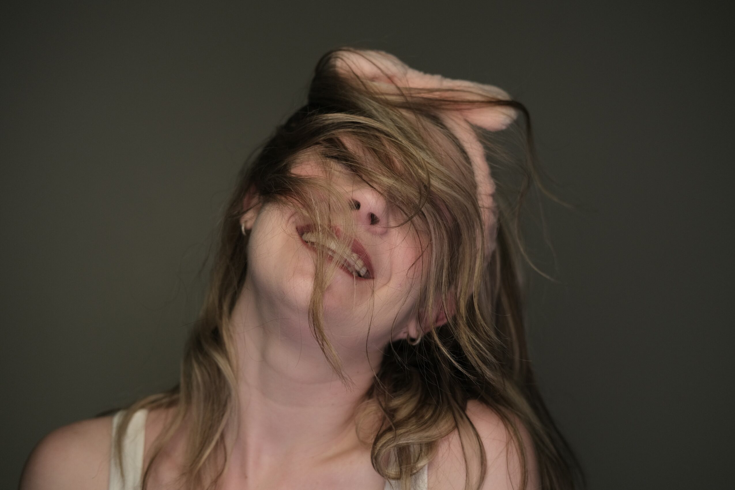 Person with long hair covering face, head tilted back, hair in motion, neutral background.