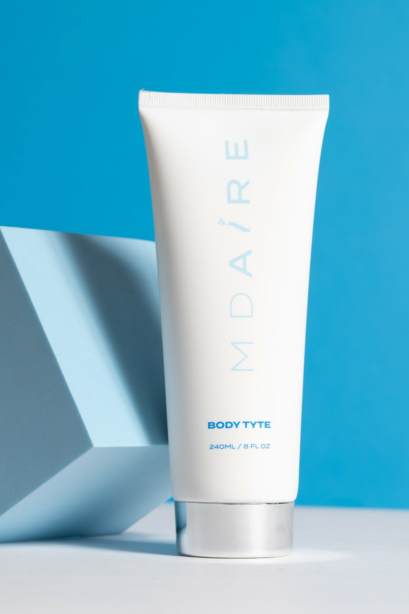 White tube with blue text on a blue background, leaning against a white geometric object.